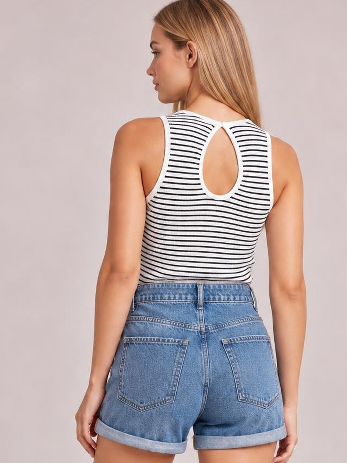 A model poses from the back in a fitted white-and-black striped ribbed round neck tank with a teardrop cutout and sleeveless silhouette.