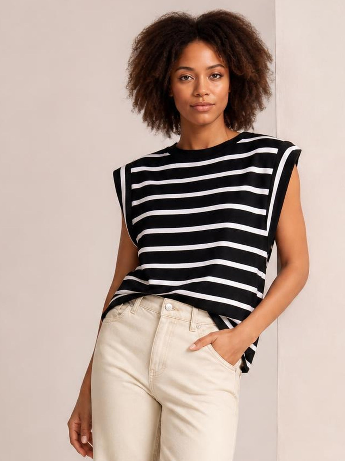 Model wearing a black and white striped round neck cap sleeve T-shirt with a relaxed silhouette, standing with one hand in her pocket.