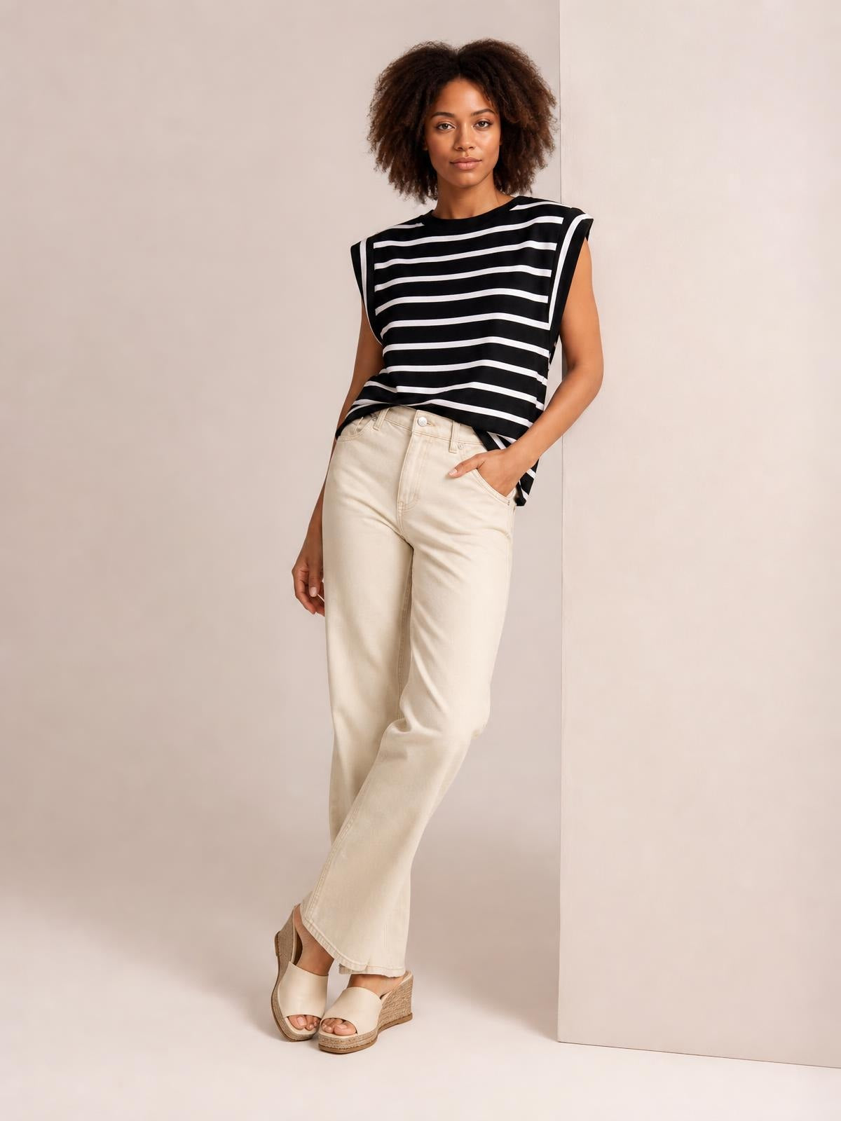 Model poses in a black-and-white striped round neck cap sleeve T-shirt with a relaxed silhouette, paired with cream wide-leg pants.