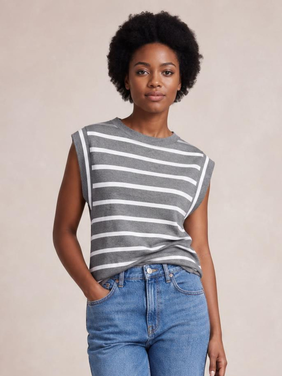 Model wearing a gray and white striped round neck cap sleeve T-shirt with a relaxed silhouette, standing with one hand in her jeans pocket.