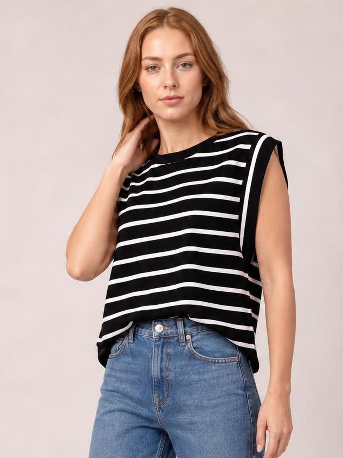 Model wearing a black-and-white striped round neck cap sleeve T-shirt with a relaxed silhouette, posing with one hand near her hair.