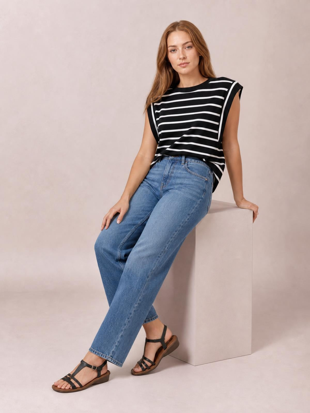 Model seated in a relaxed pose wears a black-and-white striped round neck cap sleeve T-shirt with a loose silhouette and contrast-trimmed armholes.