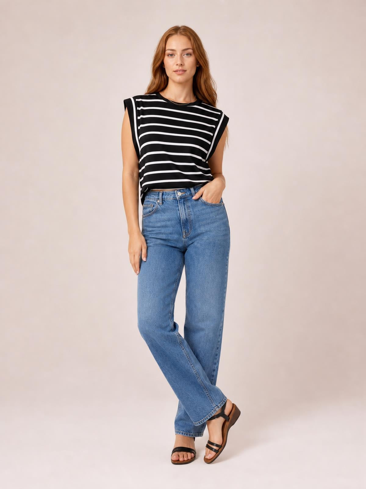 Model poses in a black-and-white striped round neck cap sleeve T-shirt with a relaxed silhouette, paired with blue jeans and one hand in a pocket.