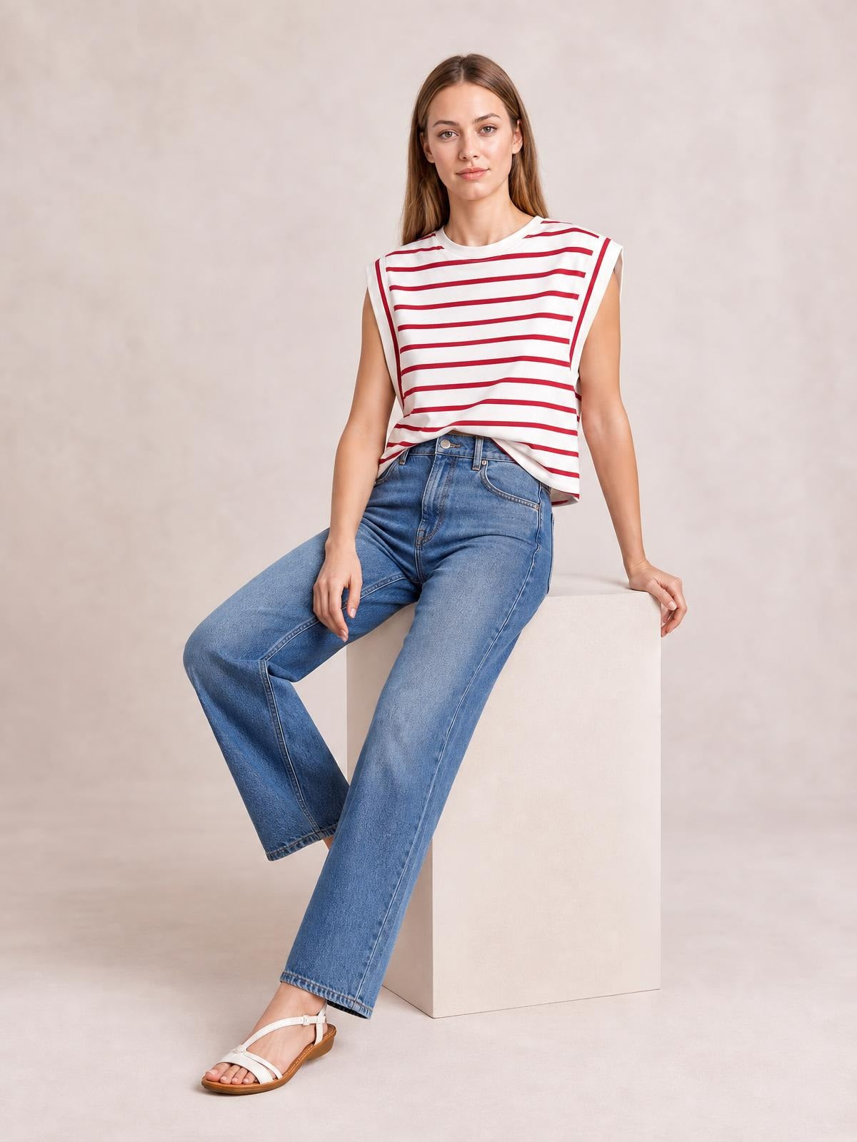 Model seated in light blue jeans wears an opaque white T-shirt with red horizontal stripes, a round neck, cap sleeves, and a relaxed silhouette.