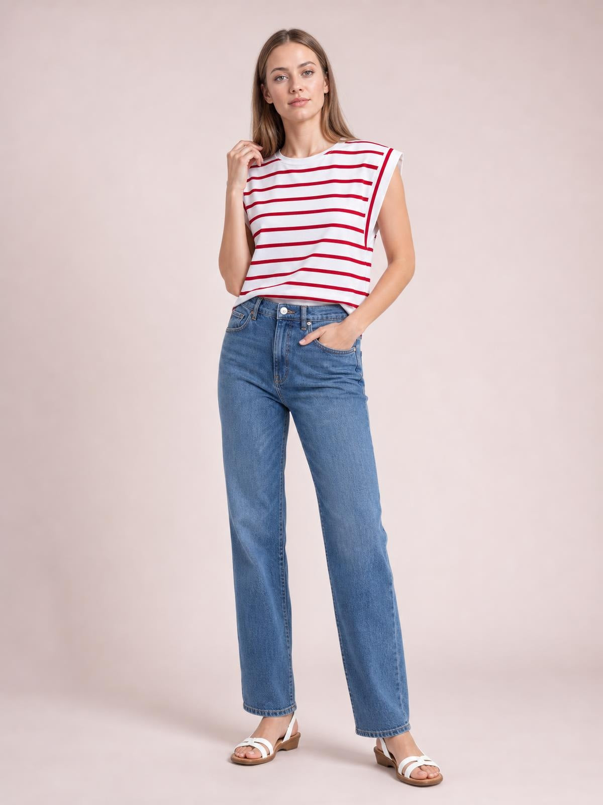 Model wearing a white striped round neck cap sleeve T-shirt with red horizontal stripes, a relaxed straight silhouette, and ribbed neckline while posing with one hand in her jeans pocket.