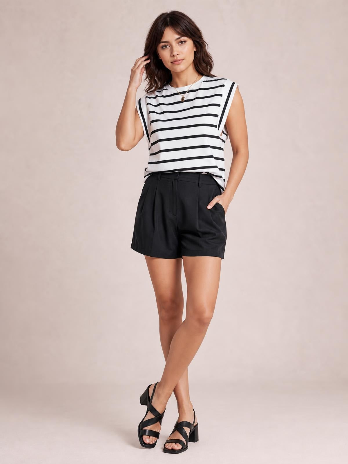 Model wearing a white and black striped round neck cap sleeve T-shirt with a relaxed silhouette, posed with one hand in her shorts pocket.
