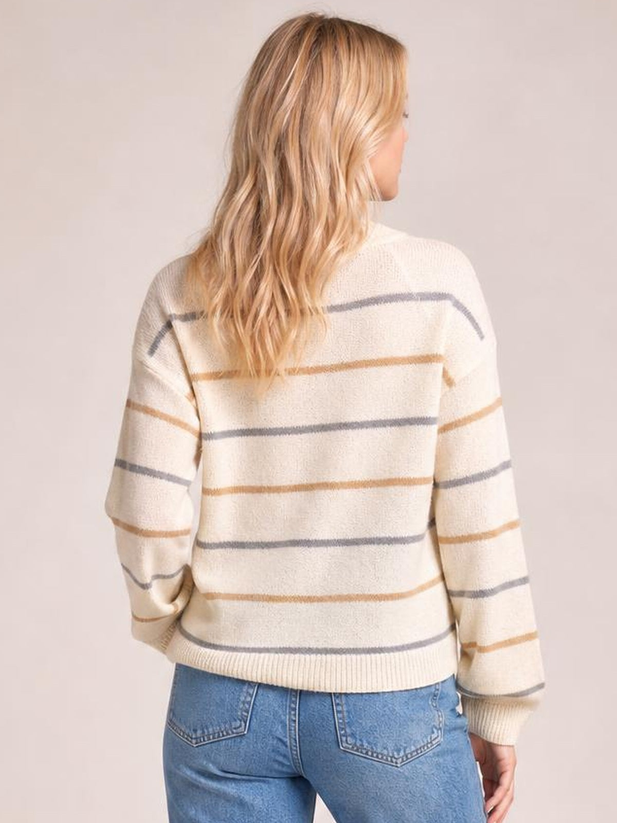 Model turned to the side and back wears a cream striped round neck sweater with drop shoulders, relaxed silhouette, long sleeves, and ribbed cuffs and hem.