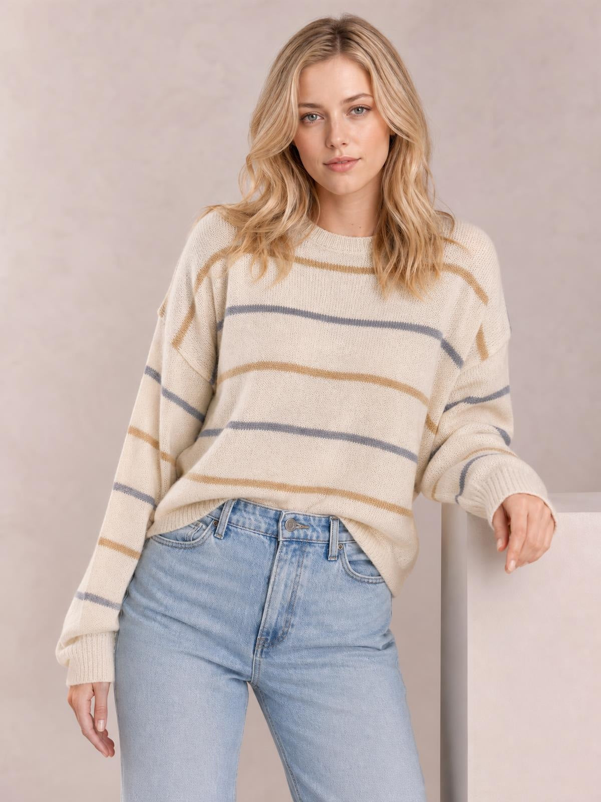 Model wears a cream striped round neck sweater with drop shoulders, relaxed silhouette, ribbed cuffs and hem, paired with light-wash jeans.