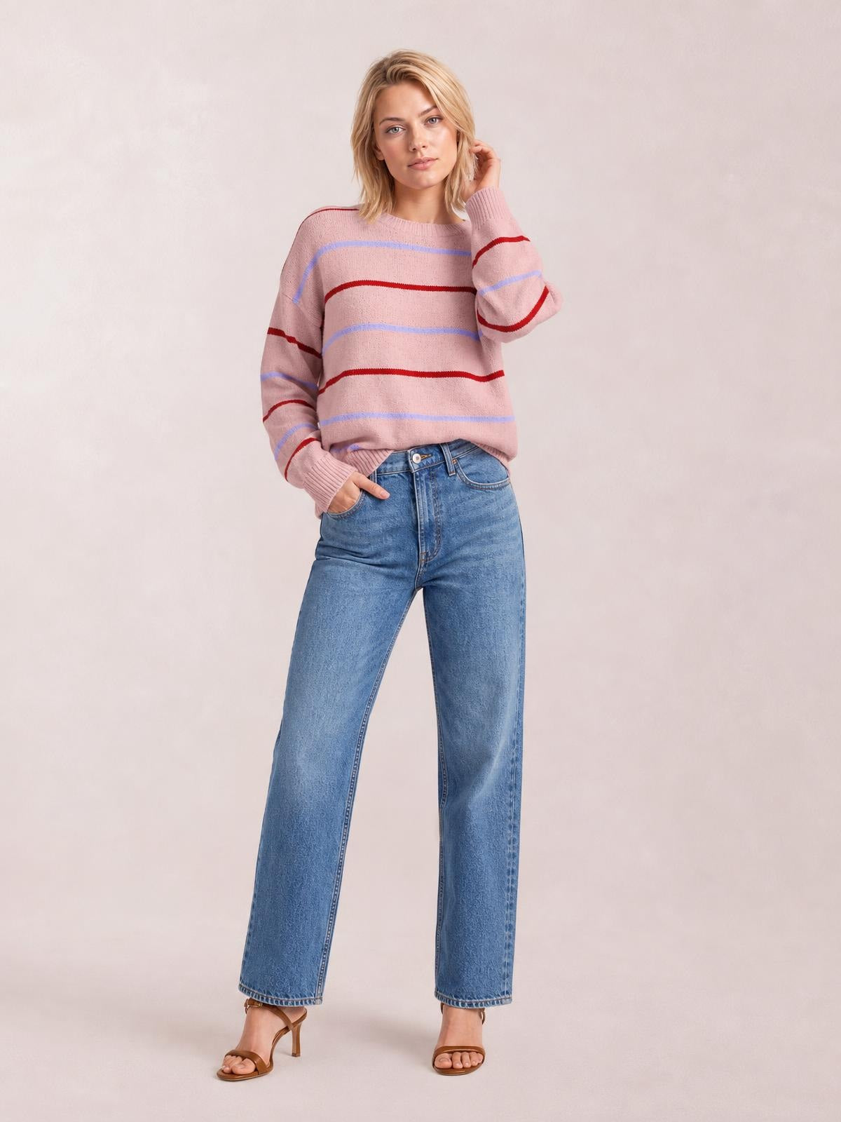 Model poses in a pink striped round neck sweater with drop shoulders, ribbed cuffs and hem, and a relaxed silhouette, paired with jeans.