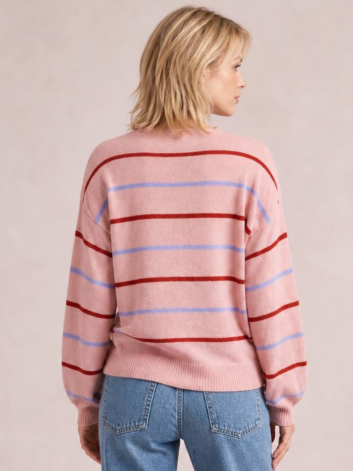 A model stands facing away in a pink striped round neck sweater with relaxed drop shoulders, long sleeves, ribbed cuffs and hem, paired with blue jeans.