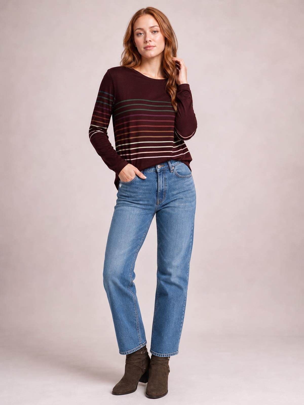 Model poses in a burgundy striped round neck long sleeve T-shirt with a relaxed silhouette, curved hem, and contrasting horizontal bands.