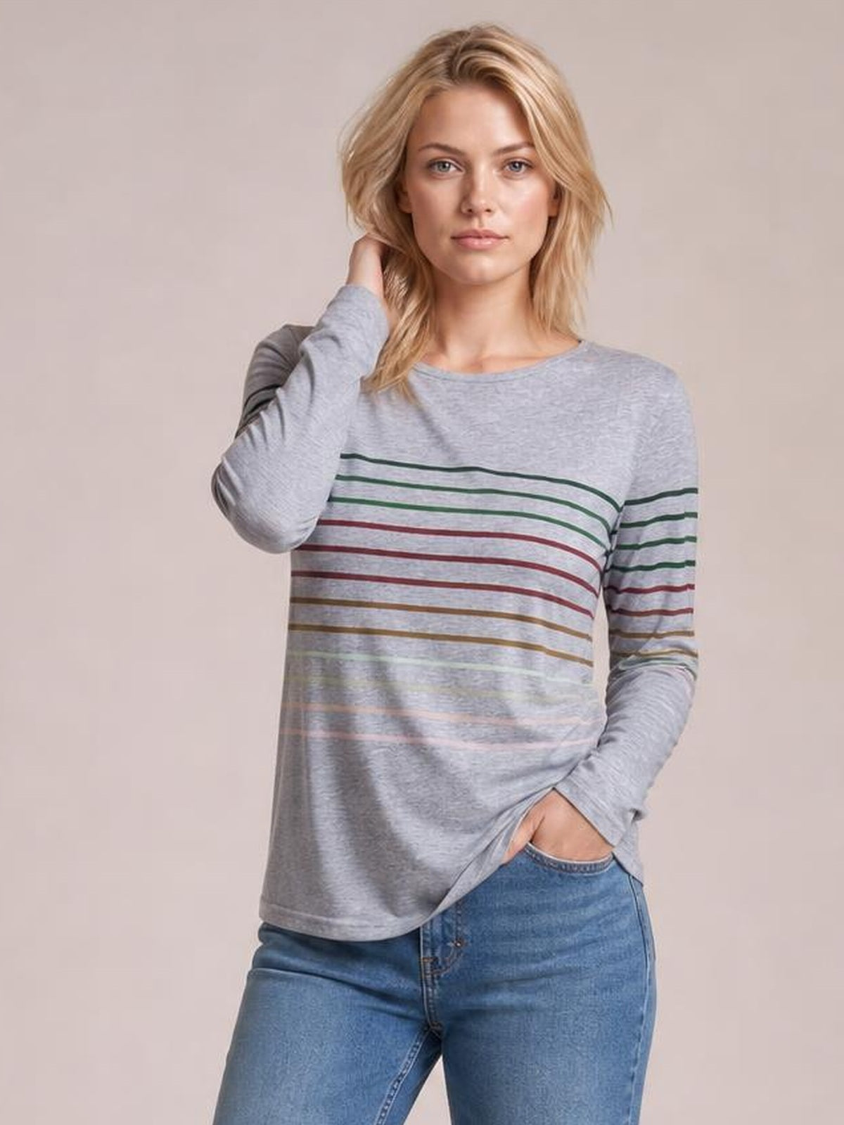 Model wearing a gray striped round neck long sleeve T-shirt with a relaxed silhouette, standing with one hand at her hair and the other in her jeans pocket.
