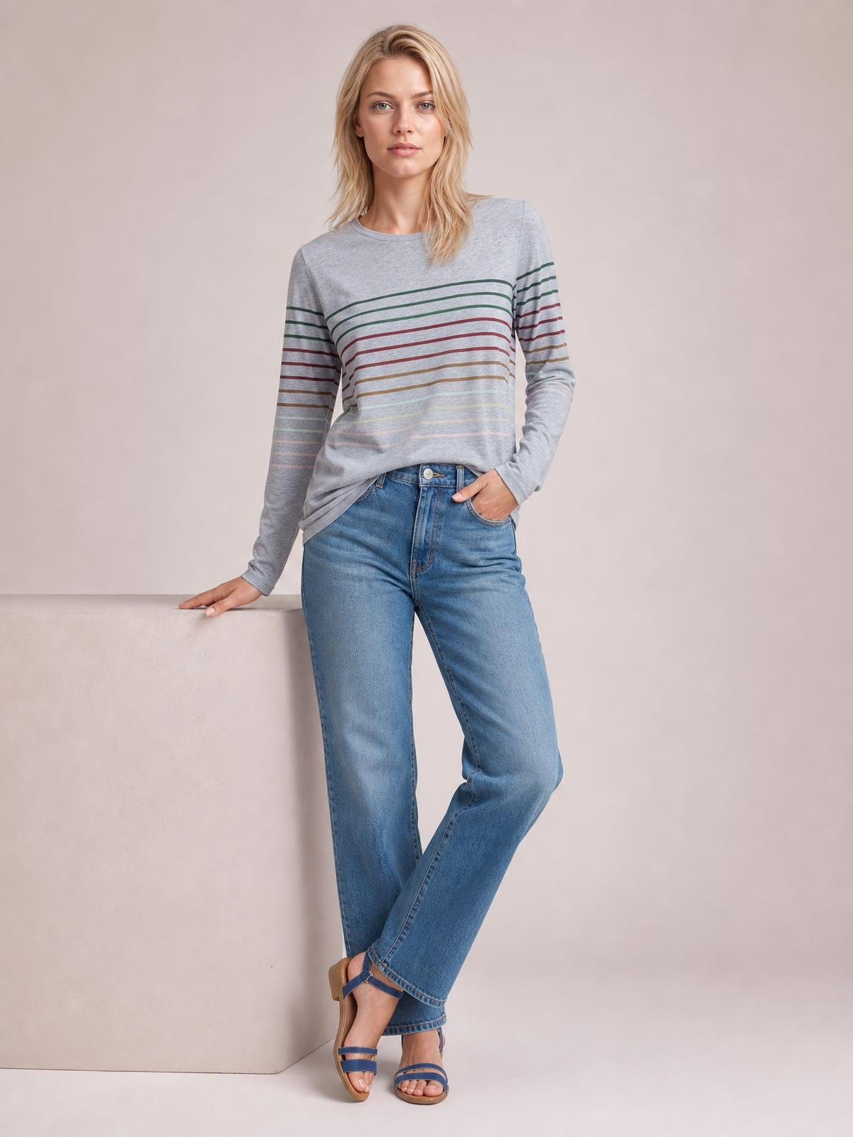 Model poses in a gray striped round neck long sleeve T-shirt with a relaxed straight silhouette, one hand in her jeans pocket and the other resting beside her.