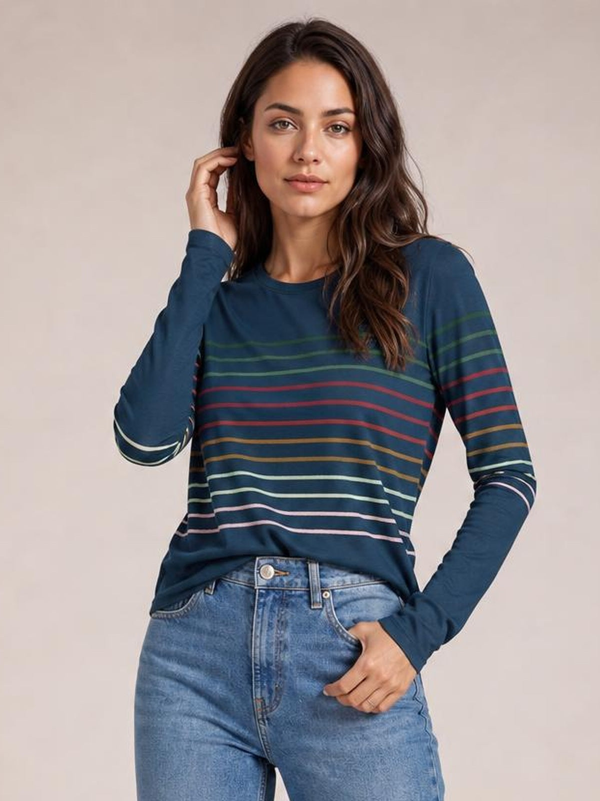 Model wearing a navy striped round neck long sleeve T-shirt with multicolor horizontal stripes, relaxed silhouette, and one hand resting near her waist.