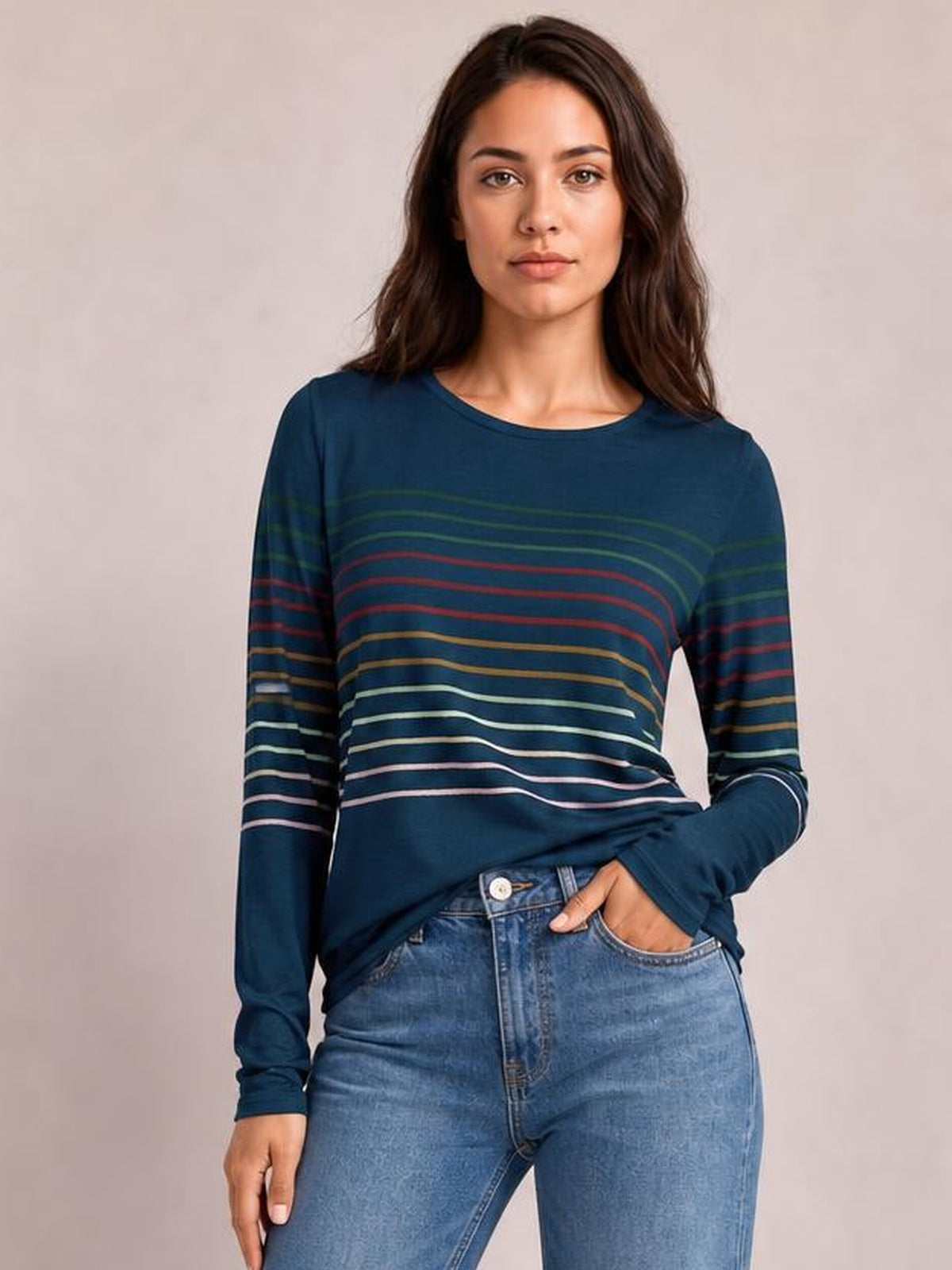 Model wearing a navy striped round neck long sleeve T-shirt with multicolor horizontal bands, a relaxed silhouette, and one hand resting in her jeans pocket.