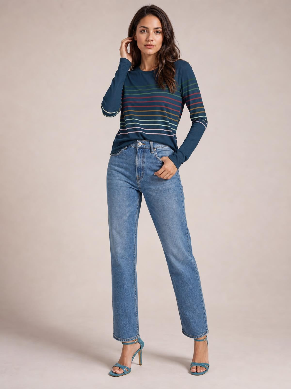 Model wearing a navy striped round neck long sleeve T-shirt with multicolor horizontal bands, a relaxed silhouette, and one hand resting at her waist.