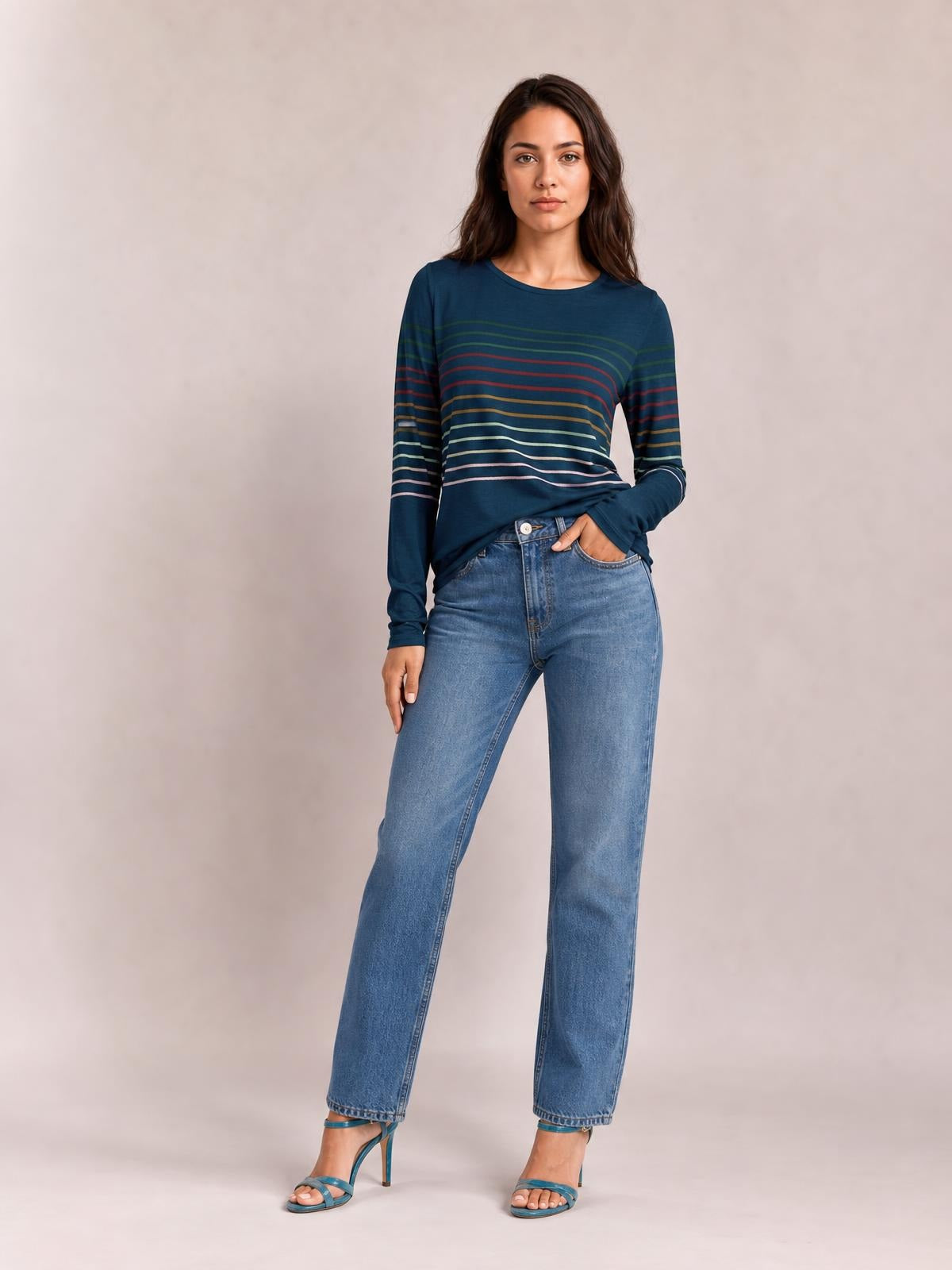 A model stands in a navy striped round neck long sleeve T-shirt with multicolored horizontal bands and a comfortable, relaxed silhouette, one hand in her pocket.