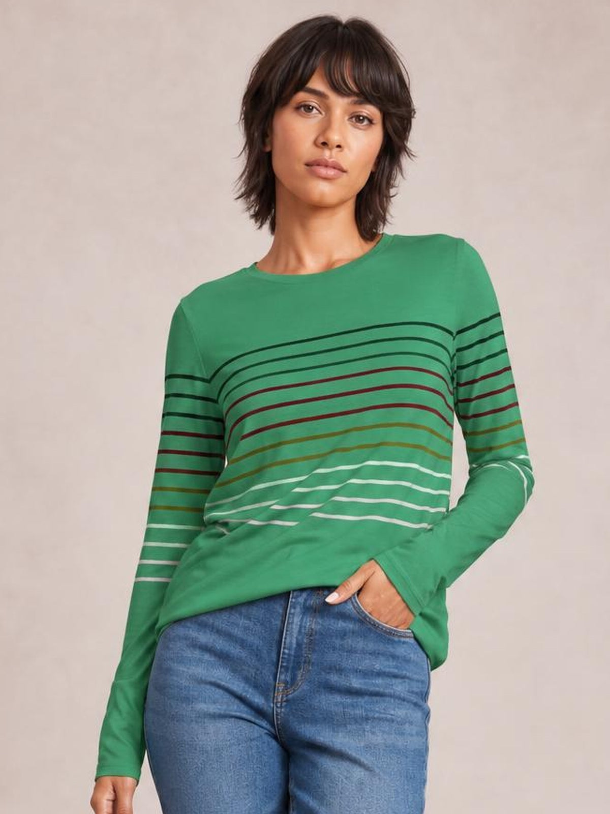 Model poses in blue jeans wearing a green striped round neck long sleeve T-shirt with a relaxed silhouette and multicolor horizontal stripe construction.