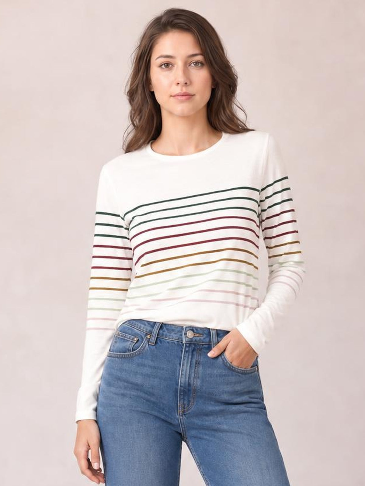 Model wearing an opaque white striped round neck long sleeve T-shirt with a relaxed silhouette, standing with one hand in her jeans pocket.