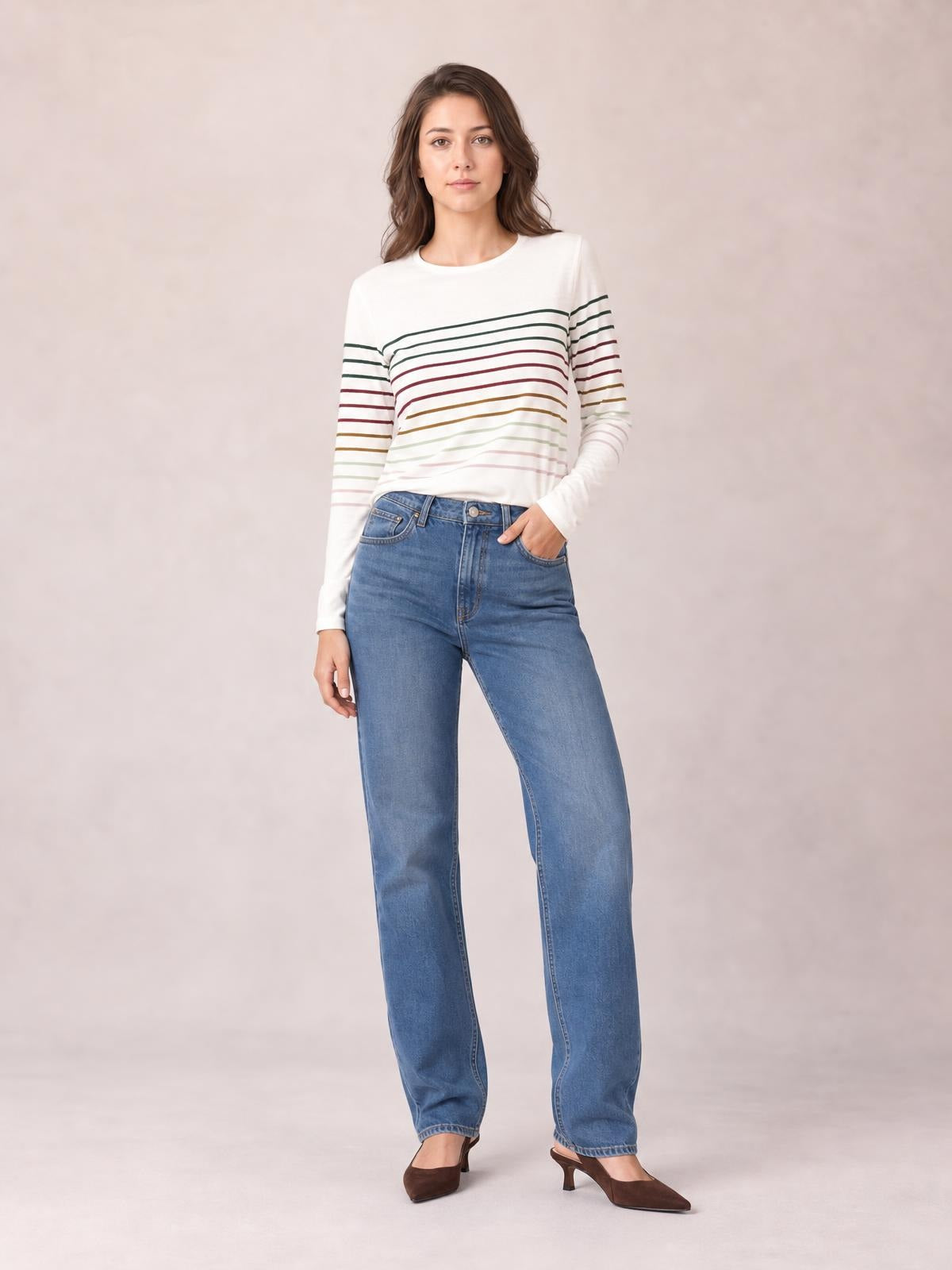 Model poses in a white striped round neck long sleeve T-shirt with multicolor horizontal bands and a relaxed straight silhouette.