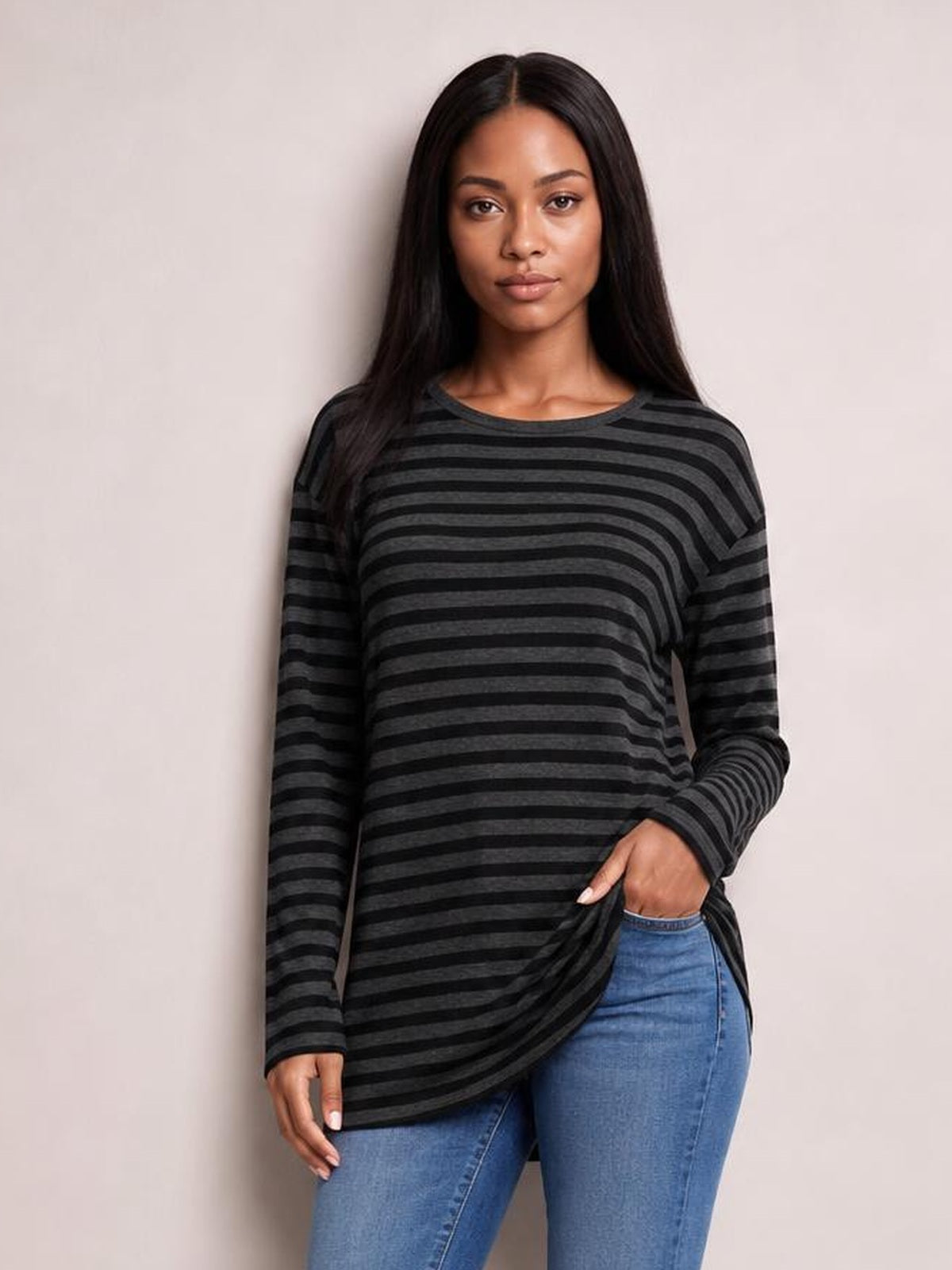 Model stands wearing a charcoal and black striped round-neck long-sleeve T-shirt with a relaxed silhouette and visible side-slit hem detail.