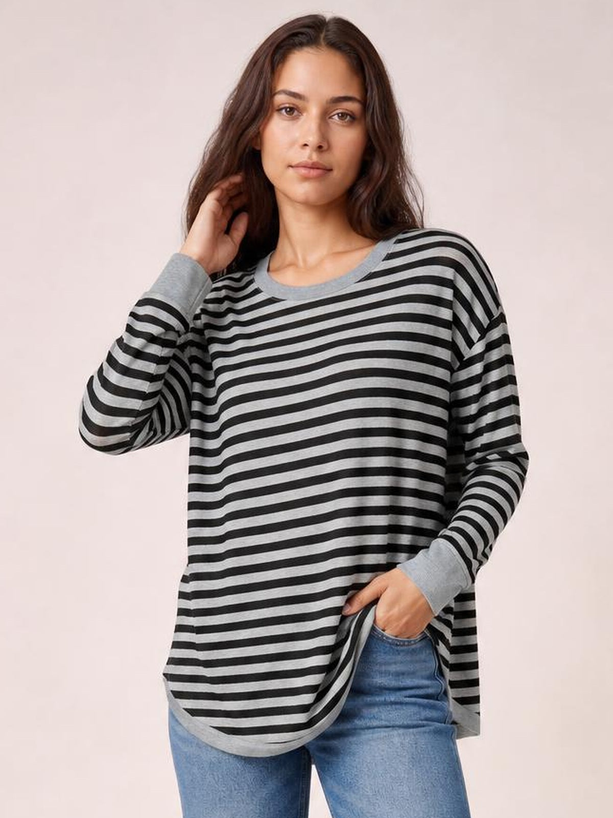 Model poses in a relaxed striped round neck long sleeve T-shirt with a loose silhouette, gray and black stripes, ribbed cuffs, and a side slit.