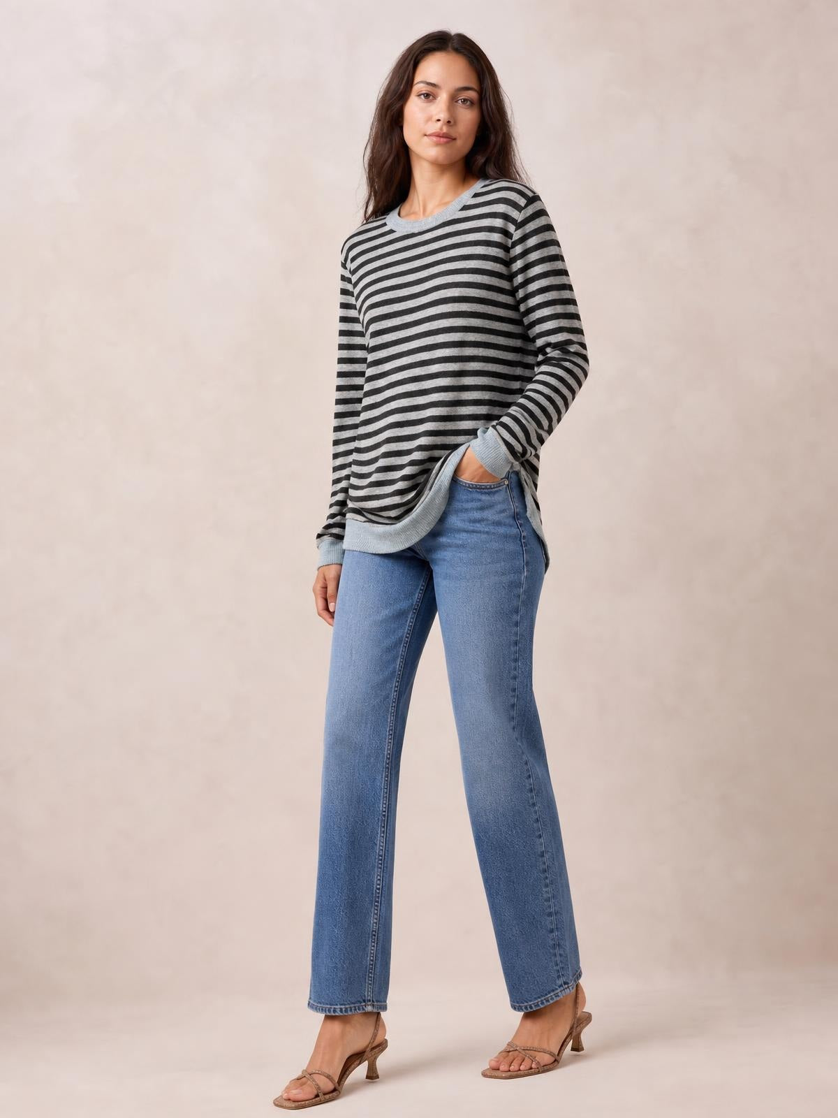 Model in a relaxed pose wears a black and gray striped round neck long sleeve T-shirt with ribbed trim and a side slit detail.
