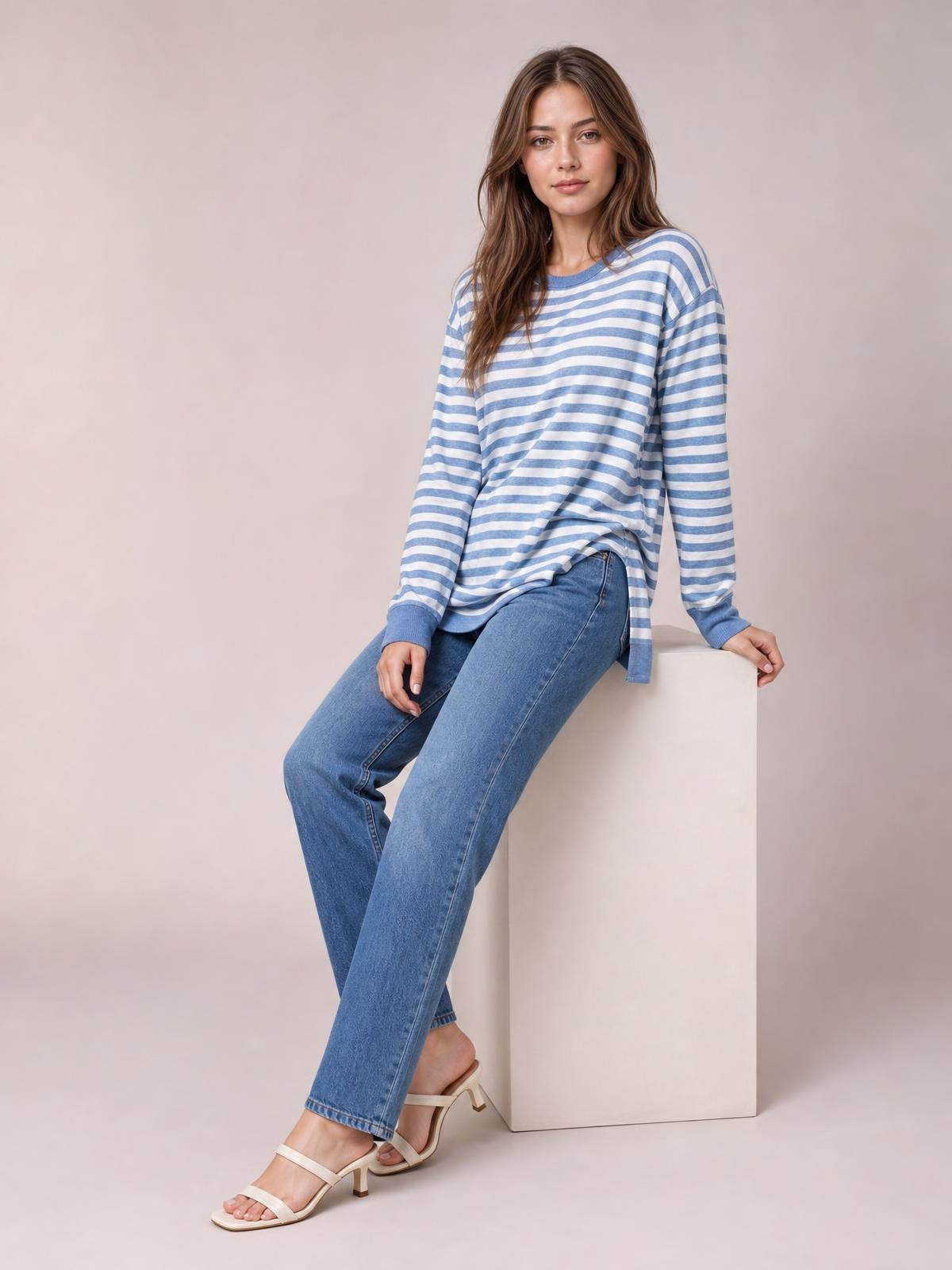 A model sits wearing a blue-and-white striped round neck long sleeve T-shirt with a relaxed silhouette and side slit detail.