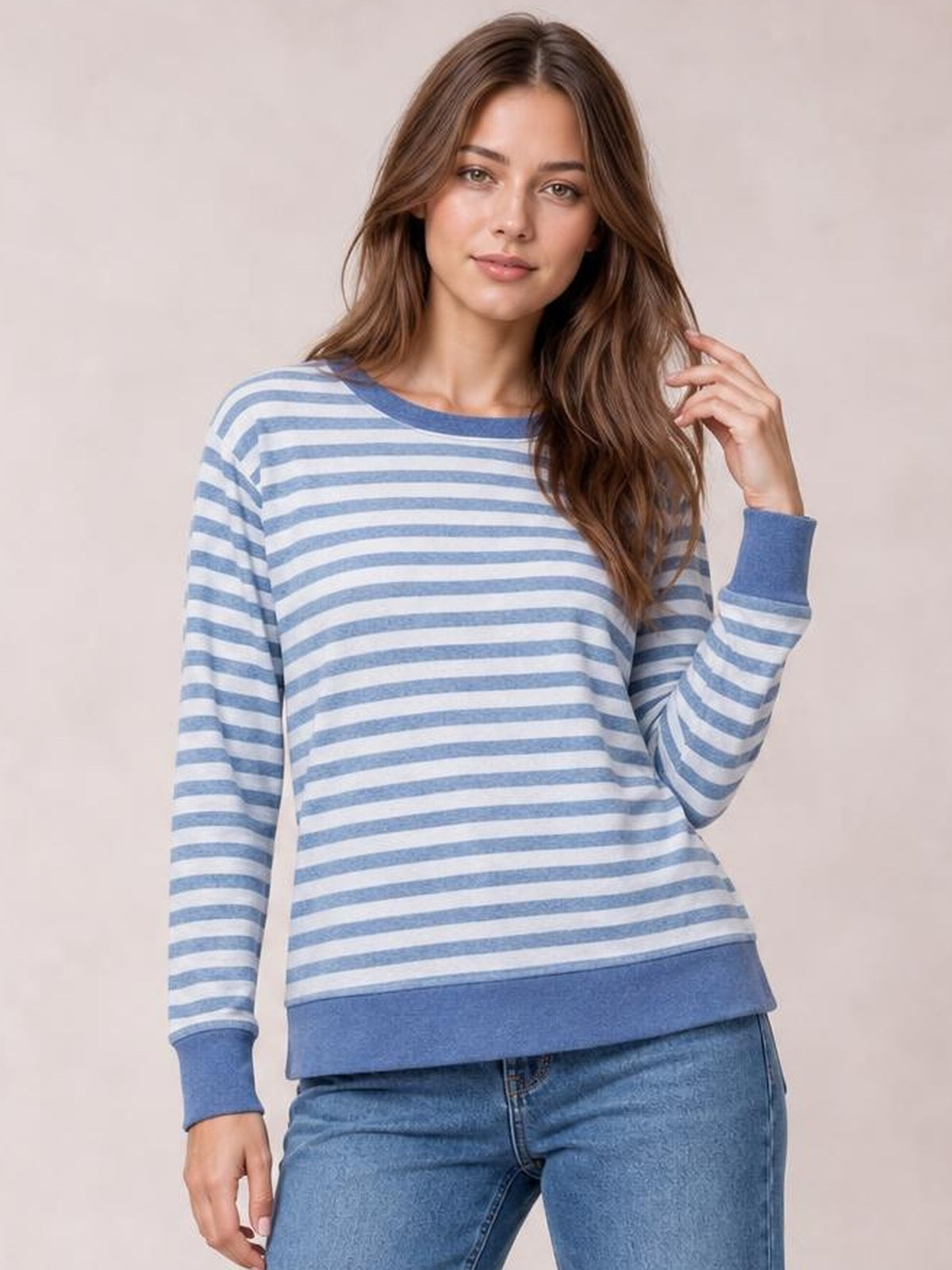 Model wearing a blue and white striped round neck long sleeve T-shirt with a relaxed silhouette, ribbed cuffs and hem, and a hand-to-hair pose.
