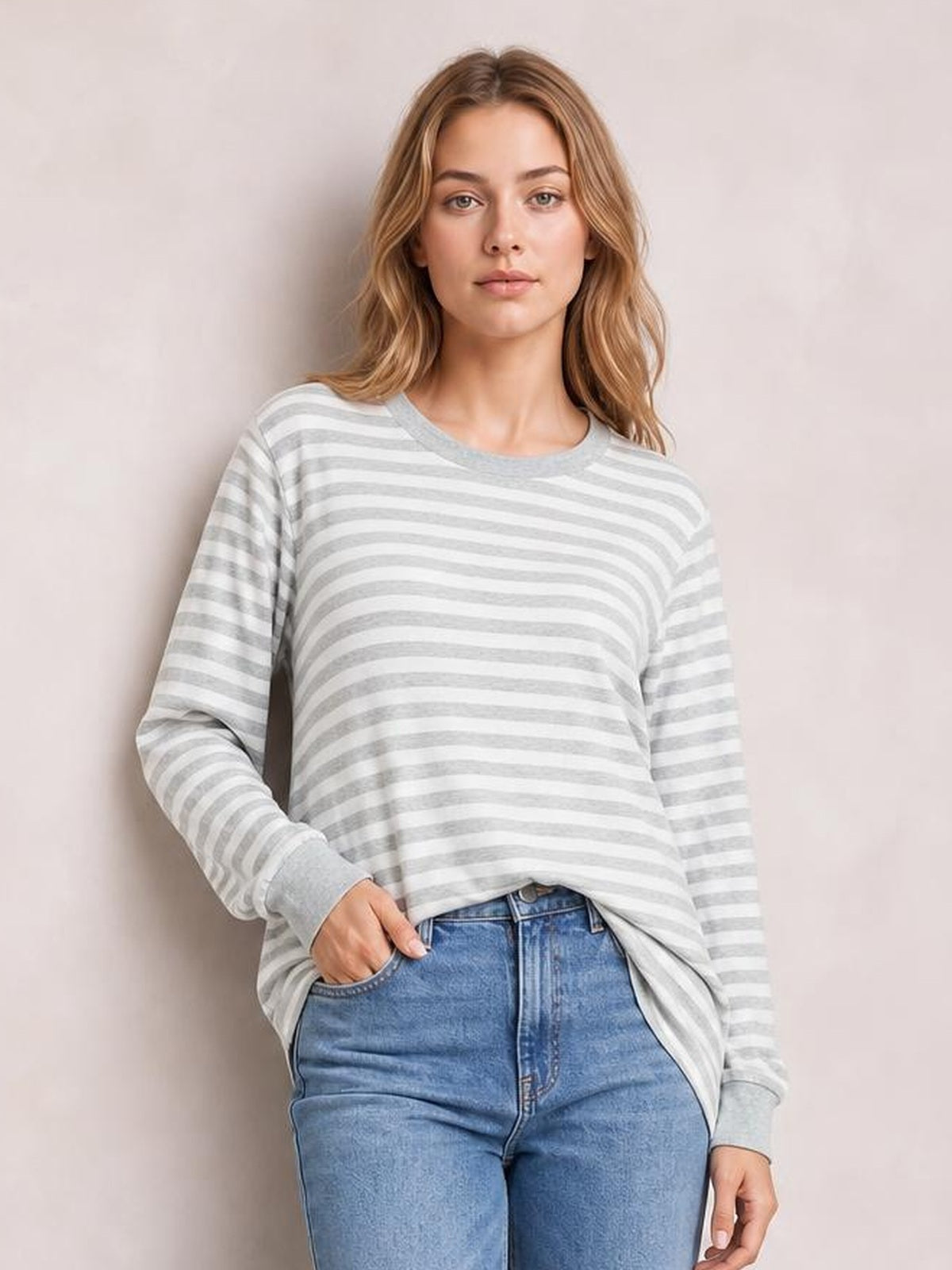 Model poses with one hand in her jeans pocket wearing an opaque gray-and-white striped round-neck long-sleeve T-shirt with a relaxed silhouette and side slit.