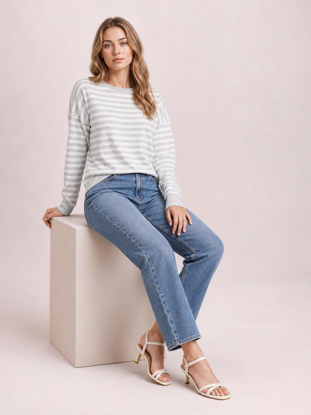 A seated model wears an opaque white and light gray striped round neck long sleeve T-shirt with a relaxed silhouette and visible side slit detail.