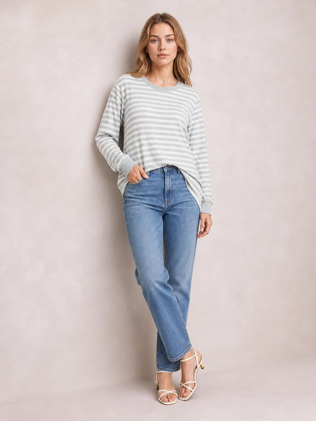 A model stands with one hand in her jeans pocket wearing a light gray and white striped round-neck long-sleeve T-shirt with a relaxed silhouette and side slit.