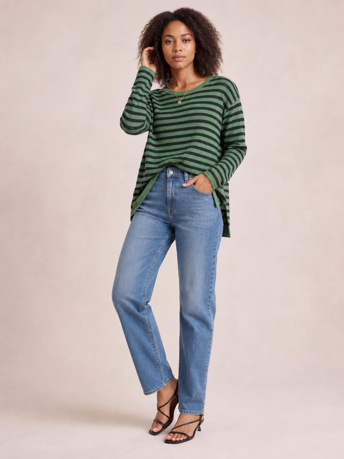 Model wearing a green and black striped round neck long sleeve T-shirt with a relaxed silhouette and visible side slit detail, posing with one hand in her pocket.