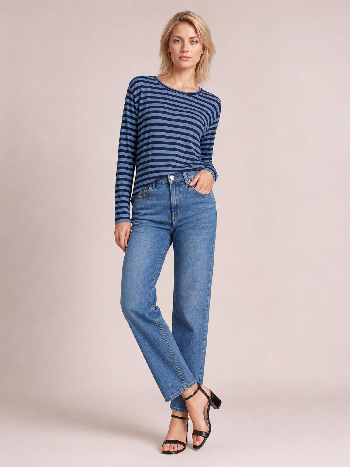 Model wearing a navy and blue striped round neck long sleeve T-shirt with a subtle slit detail, relaxed silhouette, and one hand in her pocket.