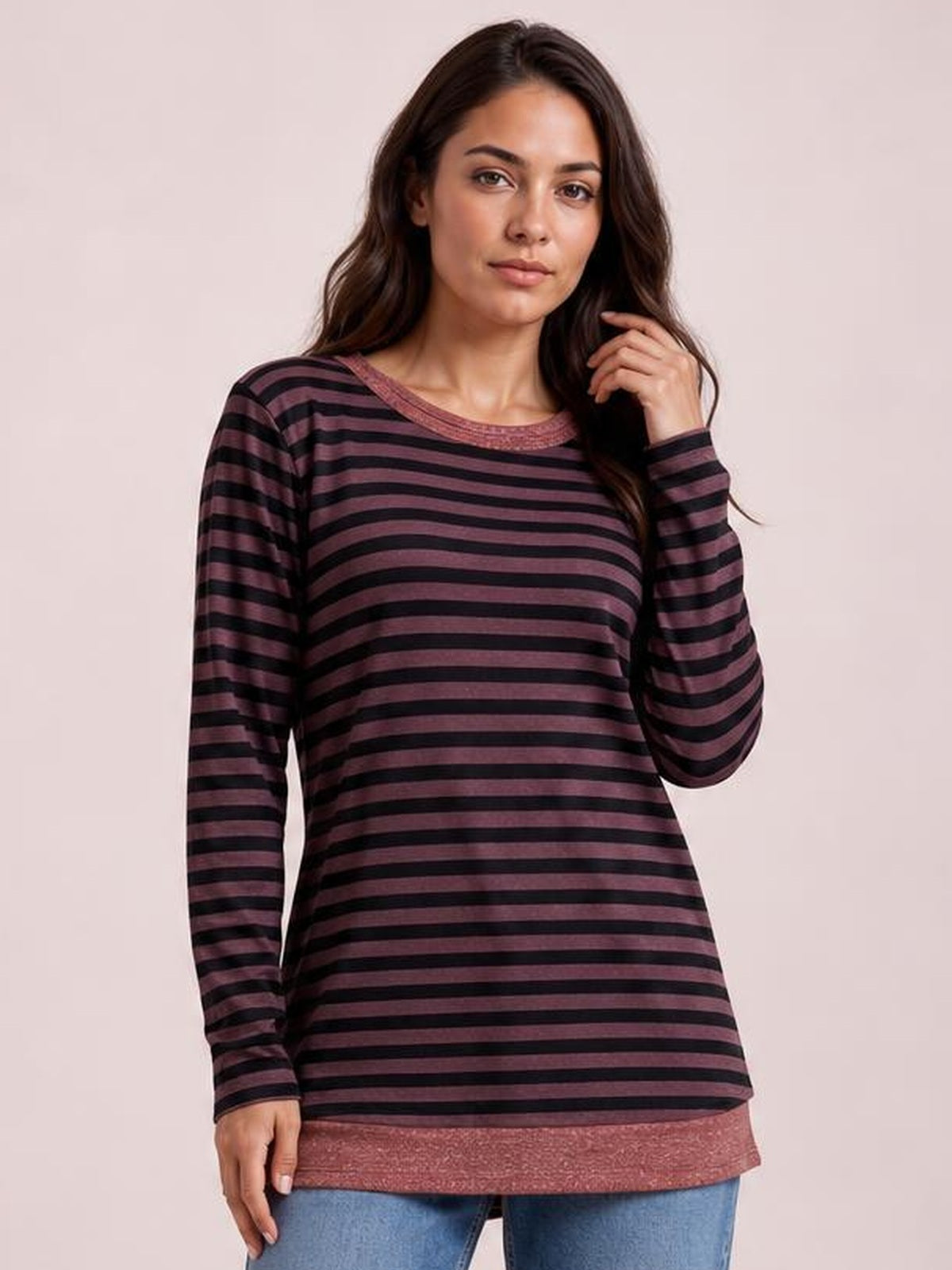 Model wears a burgundy and black striped round-neck long-sleeve T-shirt with a relaxed tunic silhouette and contrasting hem trim, touching her hair.