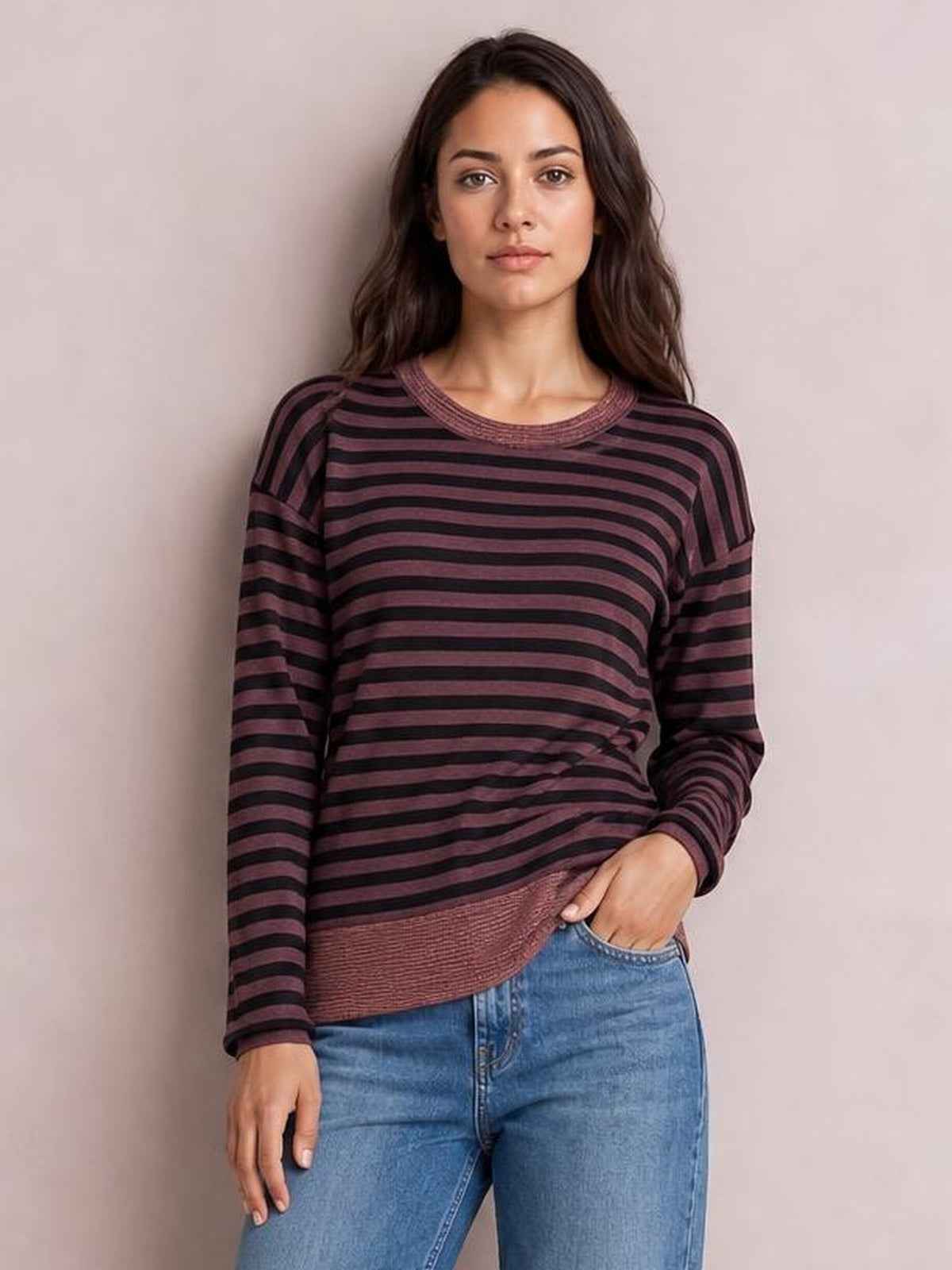 Model wearing an opaque burgundy and black striped round neck long sleeve T-shirt with a relaxed silhouette, ribbed trim, and visible slit detail.