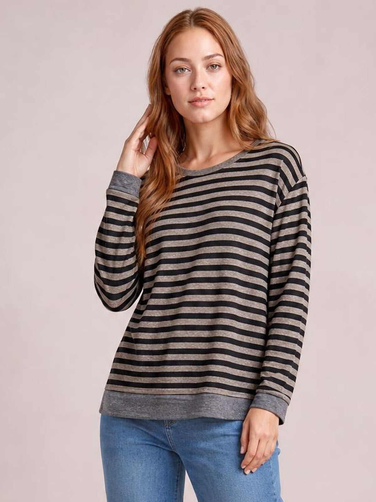Model wearing a relaxed striped round neck long sleeve T-shirt in black and gray with contrast cuffs, hem, and a casual slightly loose silhouette.