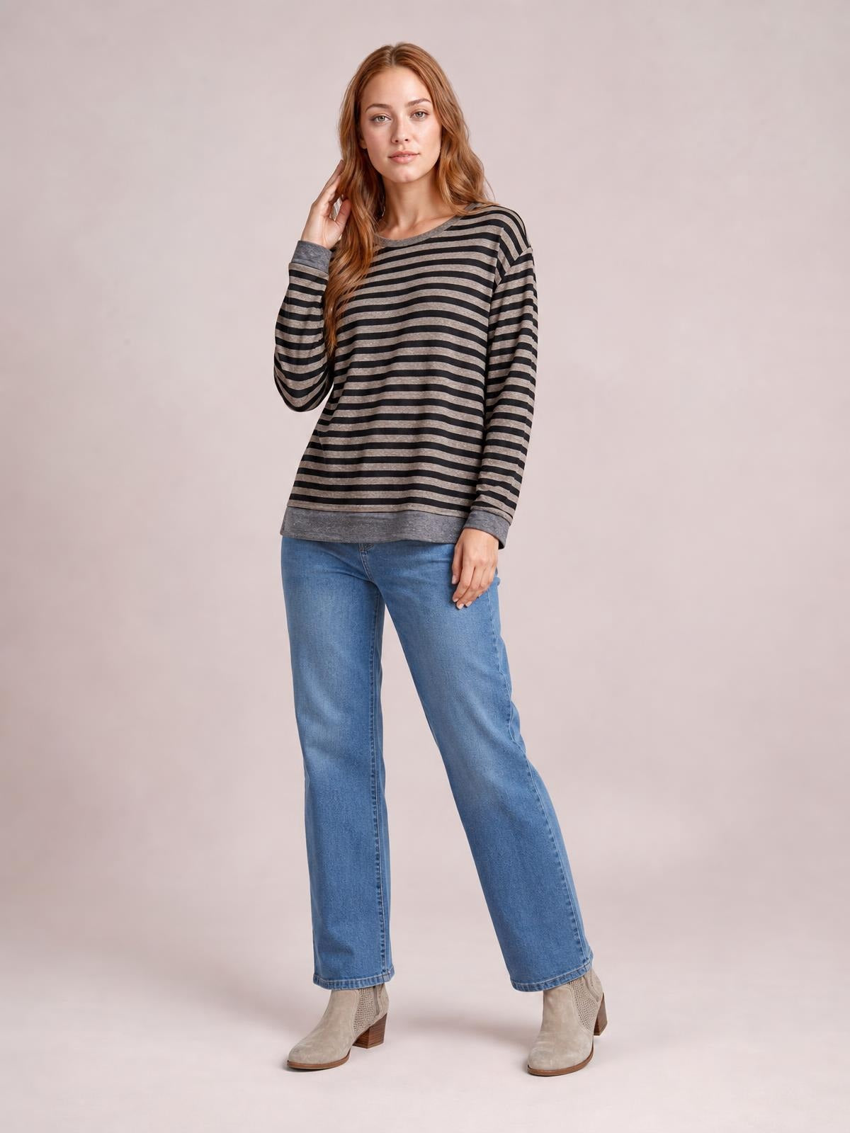 Model poses in a black and taupe striped round-neck long-sleeve T-shirt with a relaxed silhouette, contrasting gray trim, and a visible hem slit detail.