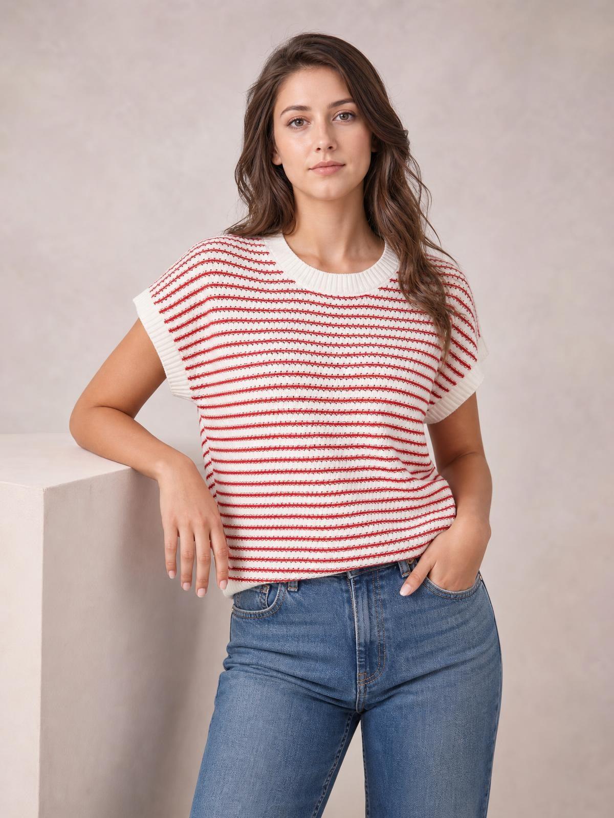 Model wearing a white and red striped round-neck short-sleeve knit top with ribbed neckline and sleeve edges, relaxed silhouette, one hand in a jeans pocket.