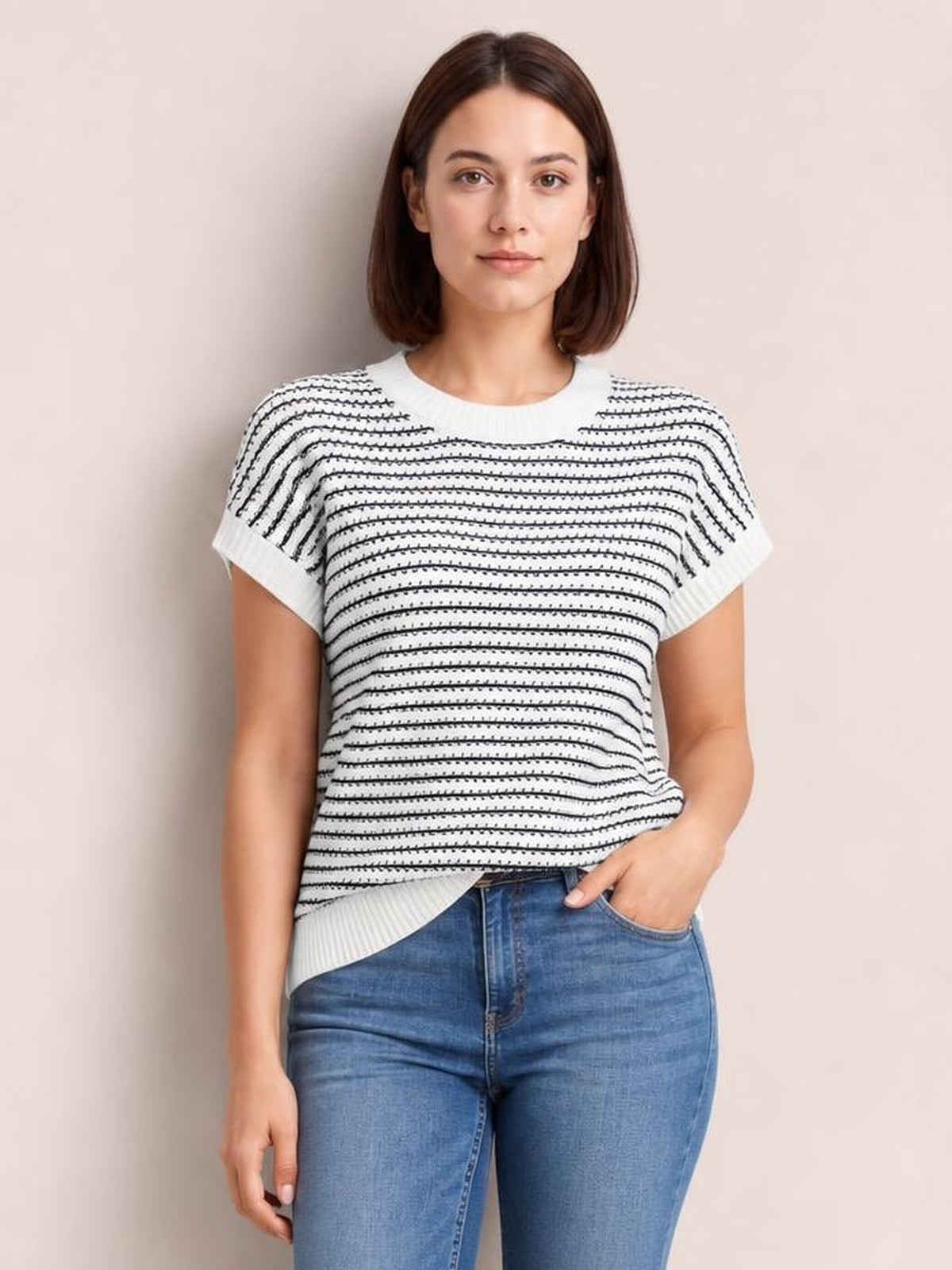 Model wearing a white striped round neck short sleeve knit top with a relaxed silhouette, ribbed neckline, cuffs, and hem, posing with one hand in her jeans pocket.