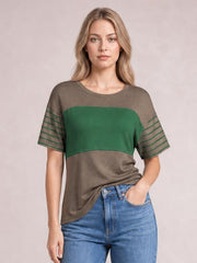 Model wearing a brown and green striped round neck short sleeve T-shirt with a relaxed silhouette, standing with one hand in her jeans pocket.