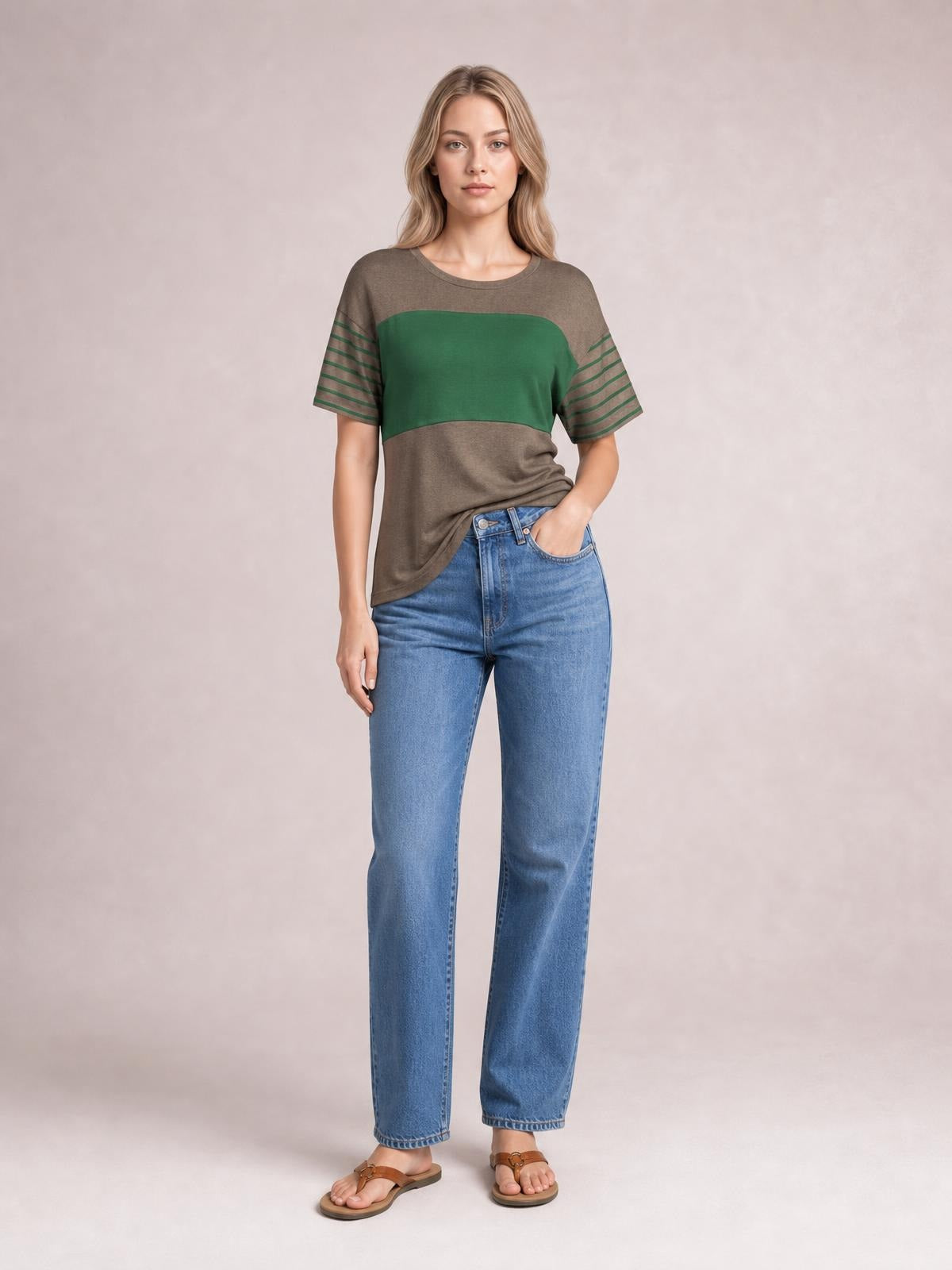 Model stands with one hand in her jeans pocket wearing a relaxed striped round-neck short-sleeve T-shirt in brown and green with striped sleeves.