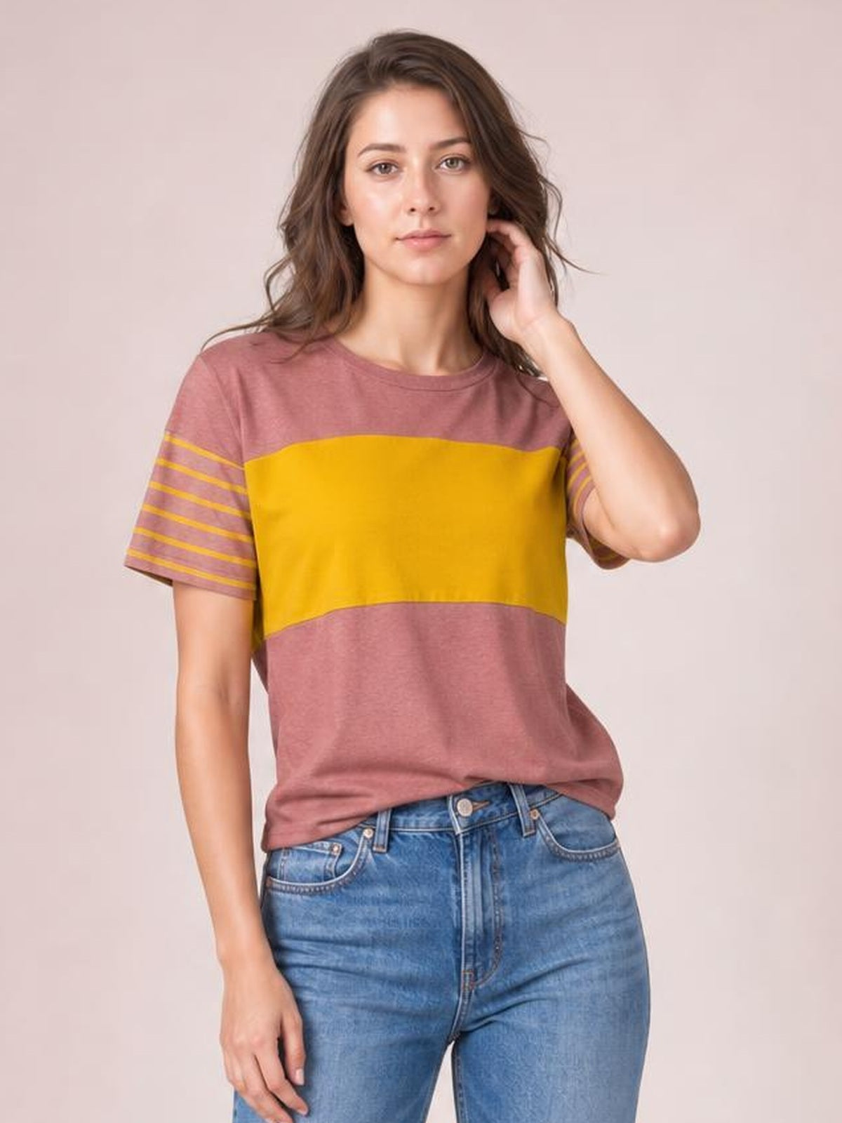 Woman posing in a striped round neck short sleeve T-shirt with mauve and mustard color-block panels and a relaxed silhouette.