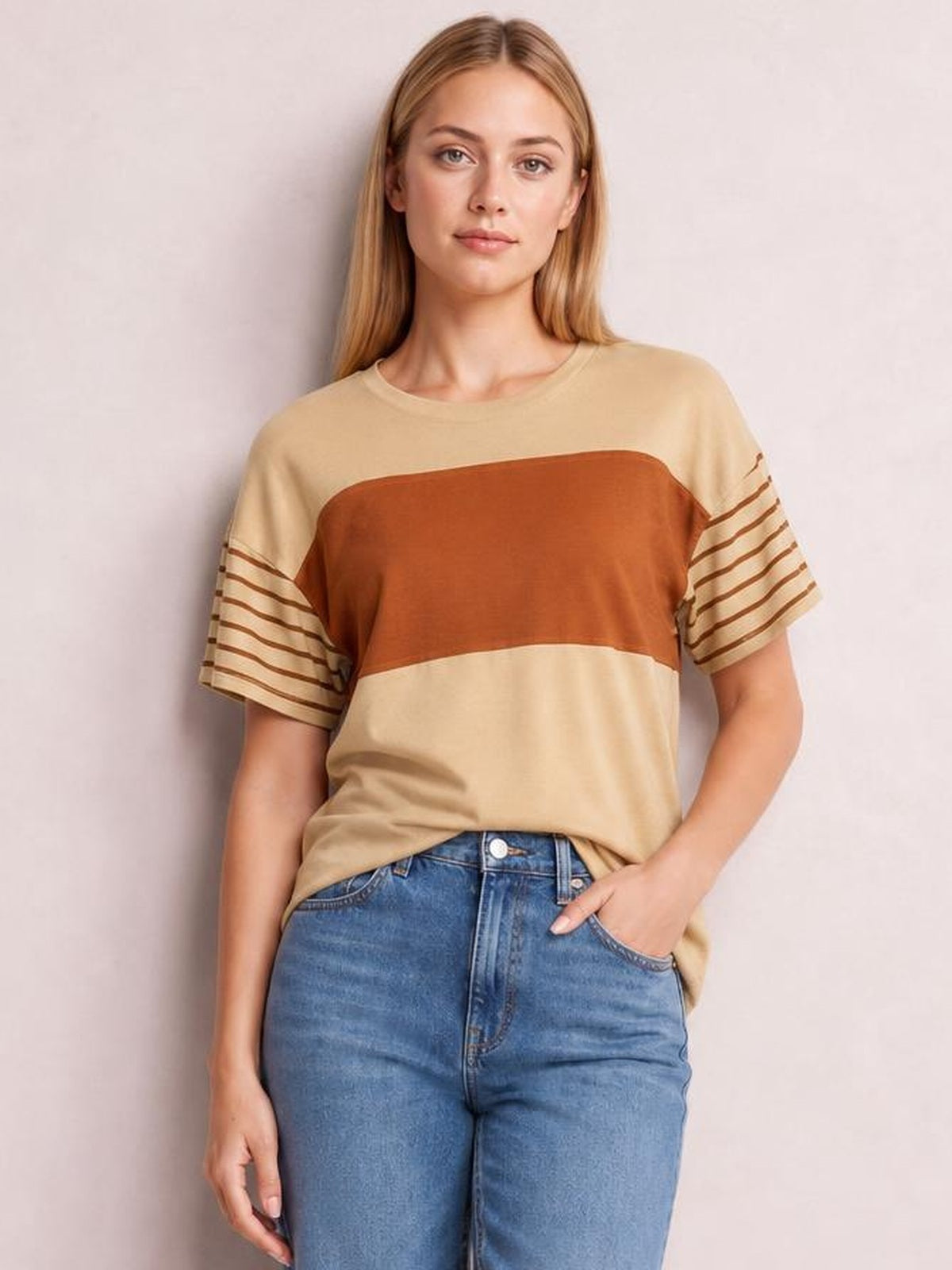 A model poses in a relaxed beige round-neck short-sleeve T-shirt with a rust color-block chest panel and striped sleeves.