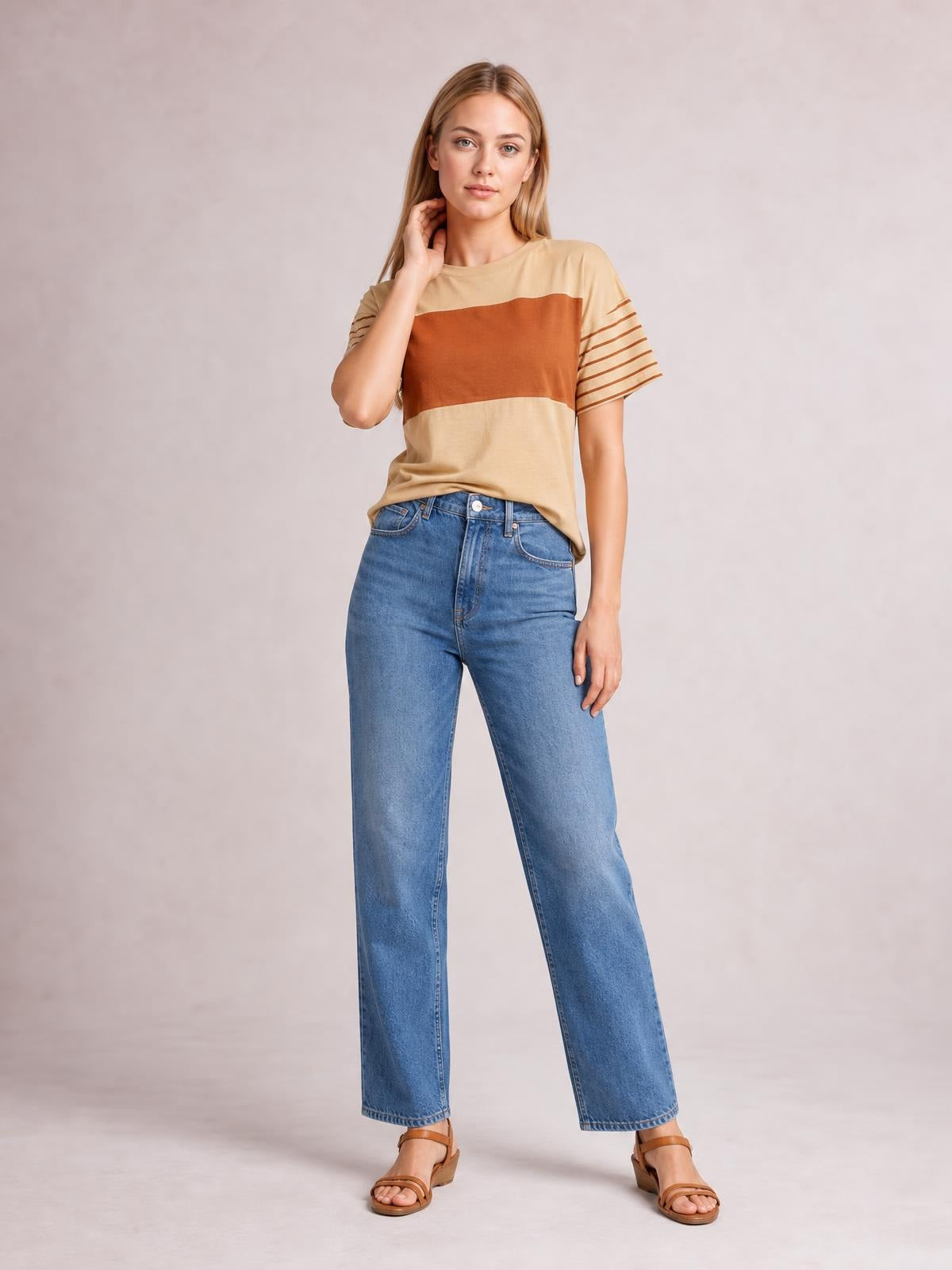A model poses in a beige striped round neck short sleeve T-shirt with rust horizontal bands, a relaxed silhouette, and contrasting linear sleeve stripes.