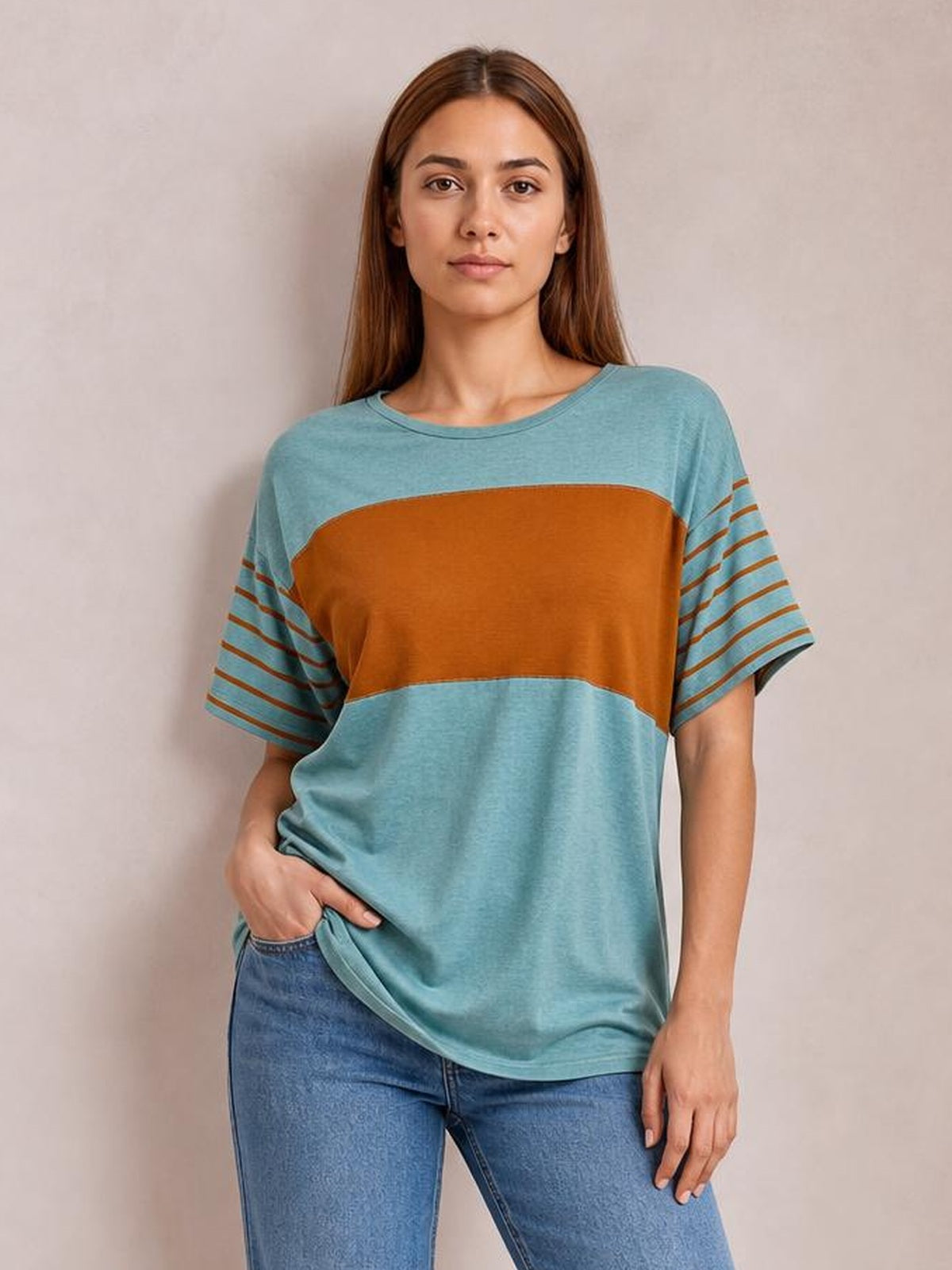 Model wearing a relaxed striped round neck short sleeve T-shirt in blue with a contrasting rust panel, gently lifting the hem while standing.
