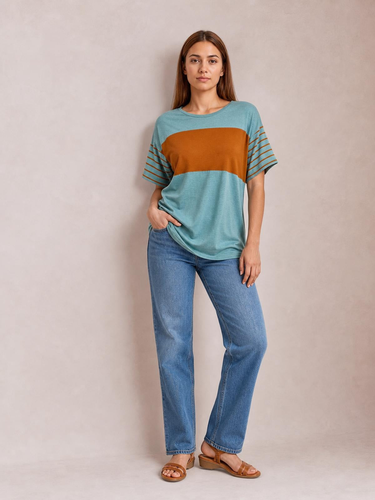 Model wears a teal and rust striped round neck short sleeve T-shirt with a relaxed silhouette, curved hem, and hand resting at the hip.