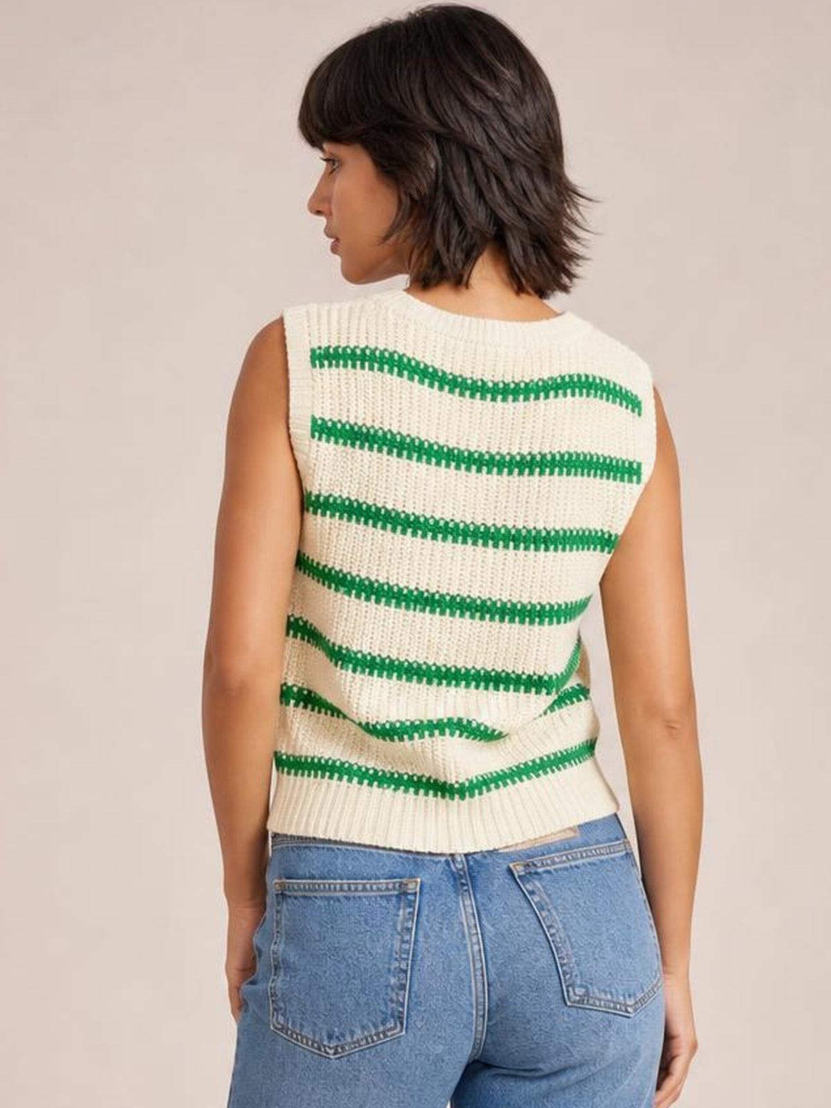 A model shows the back of a cream striped round neck sweater vest with green horizontal bands, sleeveless construction, ribbed edges, and a straight silhouette.