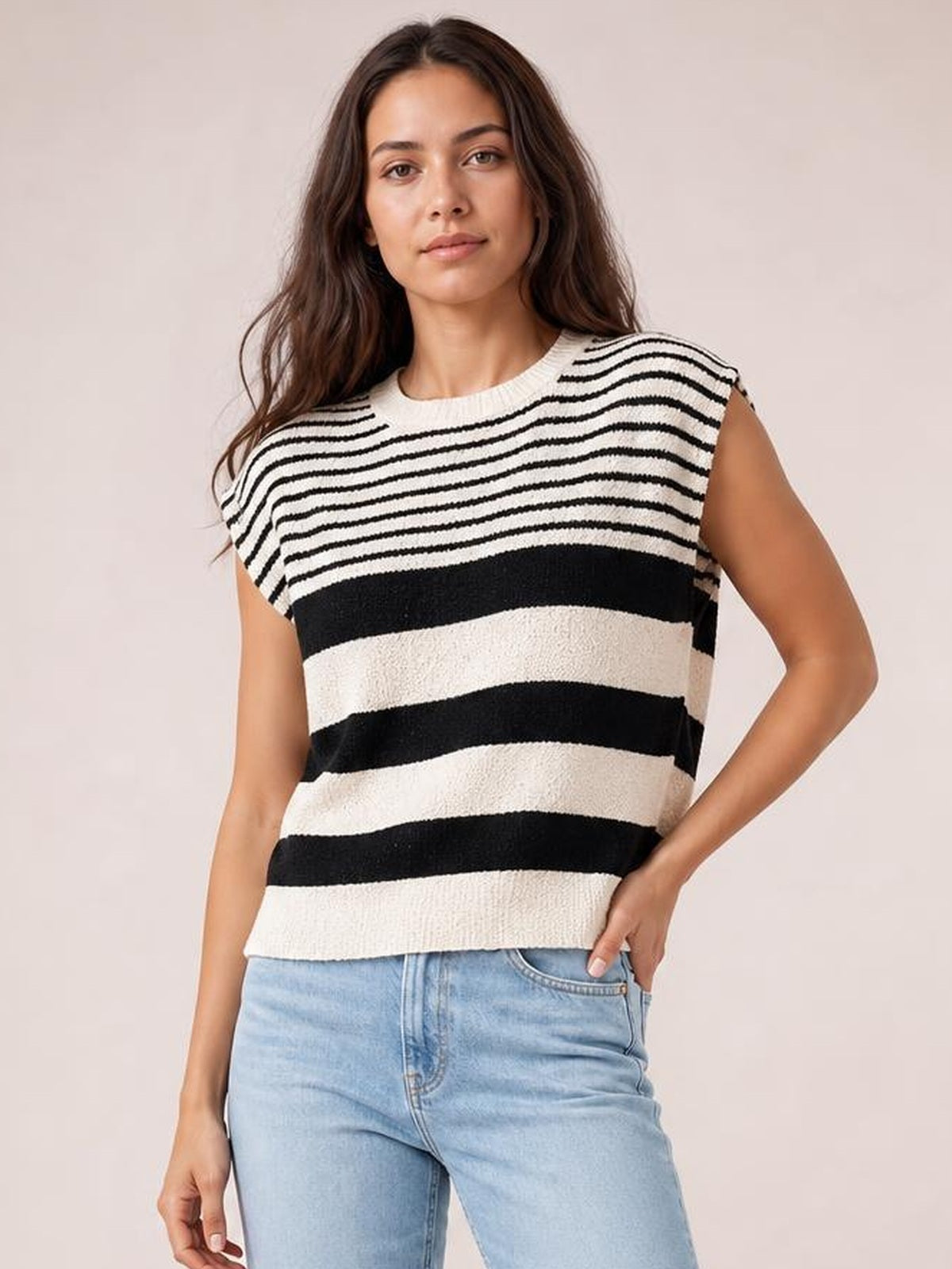 Model wearing a black-and-white striped round-neck sweater vest with a sleeveless cut and relaxed straight silhouette, posing with one hand in her jeans pocket.