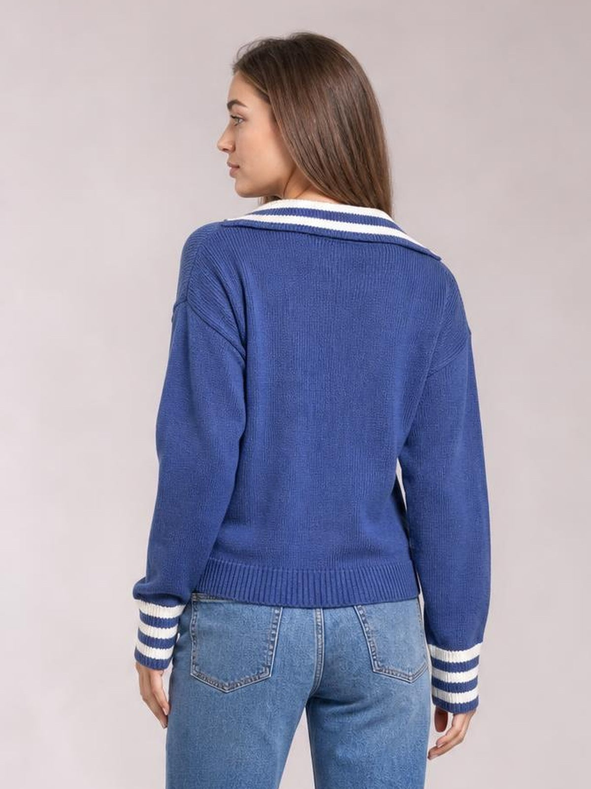 A model poses in a blue drop shoulder sweater with white striped trim at the collar and cuffs, ribbed hem, and a relaxed silhouette.